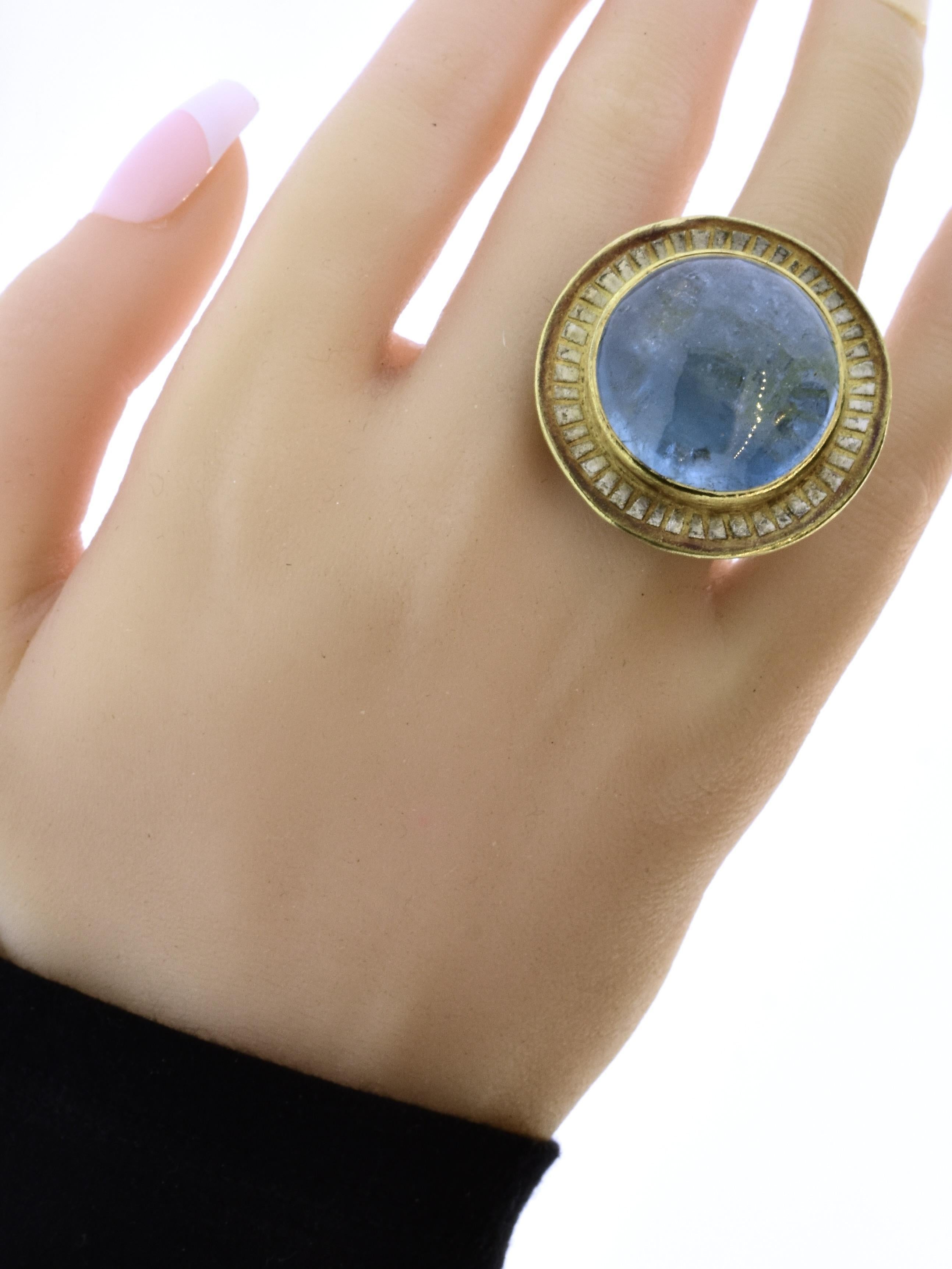 Contemporary jewelry artist Michael Zobel has hand crafted a highly unusual ring centering an approximately 47 ct. natural cabochon cut aquamarine bezel set in 18K yellow gold accented with 'rays' of oxidized sterling silver on the top and backed