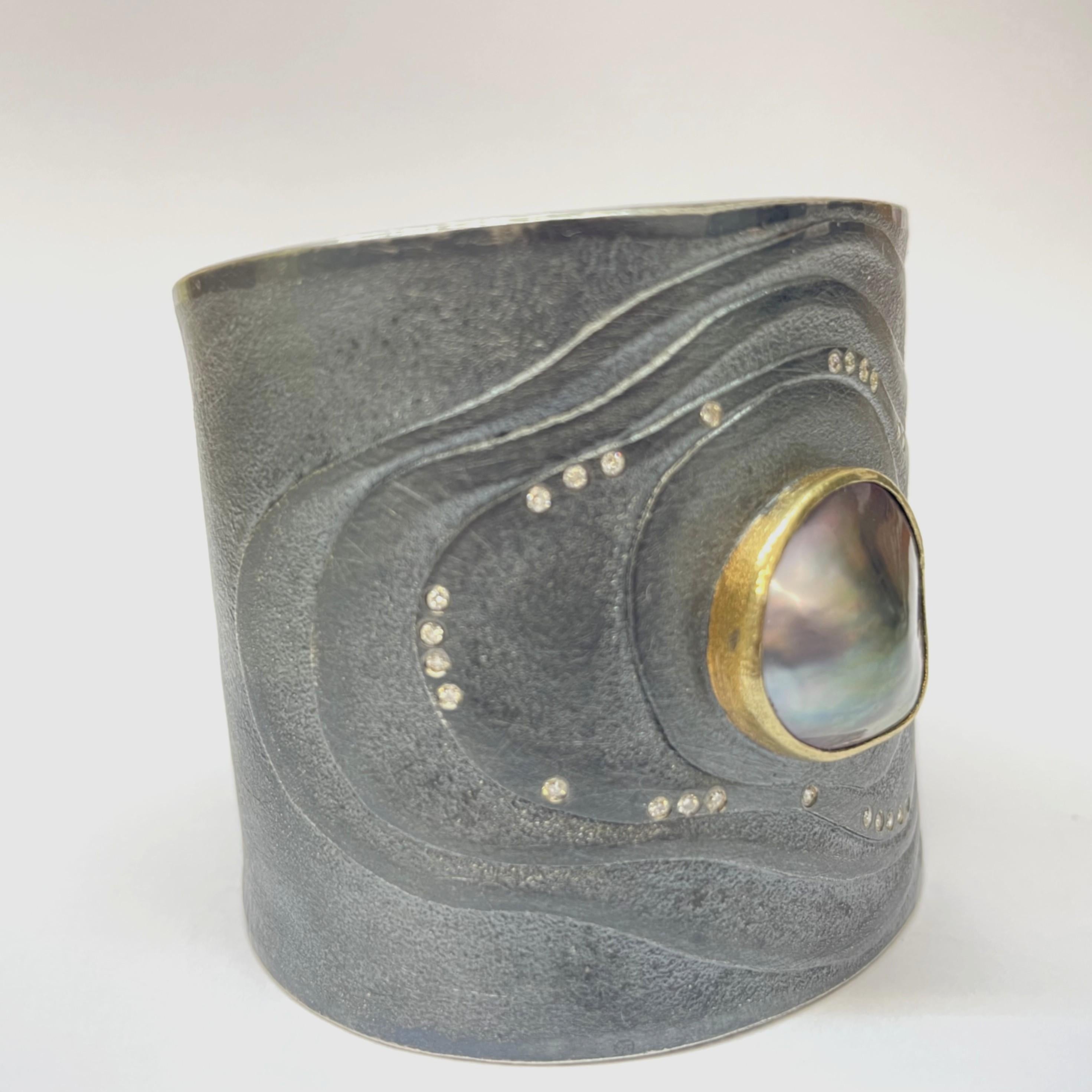 This striking cuff bracelet by Atelier Zobel is a blend of organic elegance and contemporary design. Crafted in richly textured, matt oxidized silver and hallmarked 925 (reference: ZO 221 688), the piece centers around a pink and green coloured Mabé