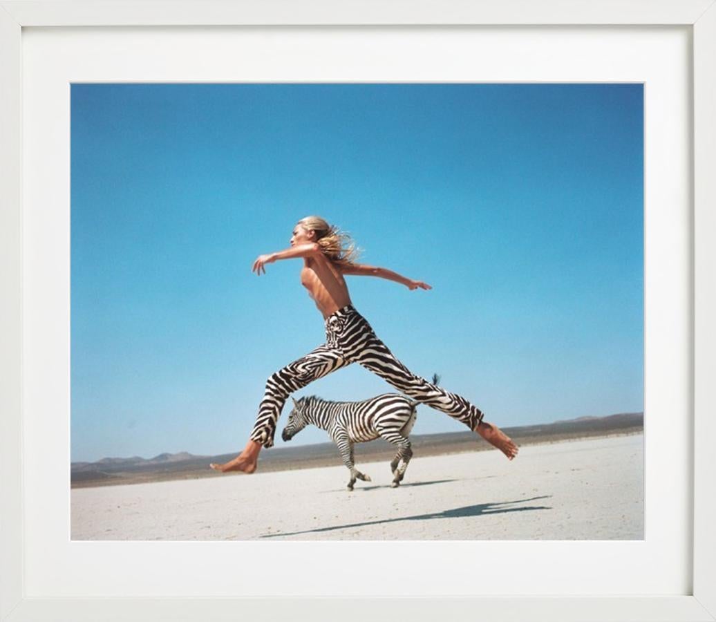 Halbnacktes Modell in einer Hose mit Zebradruck, das mit einem Zebra durch die Wüste springt, fotografiert von Michel Comte im Rahmen der Serie 
