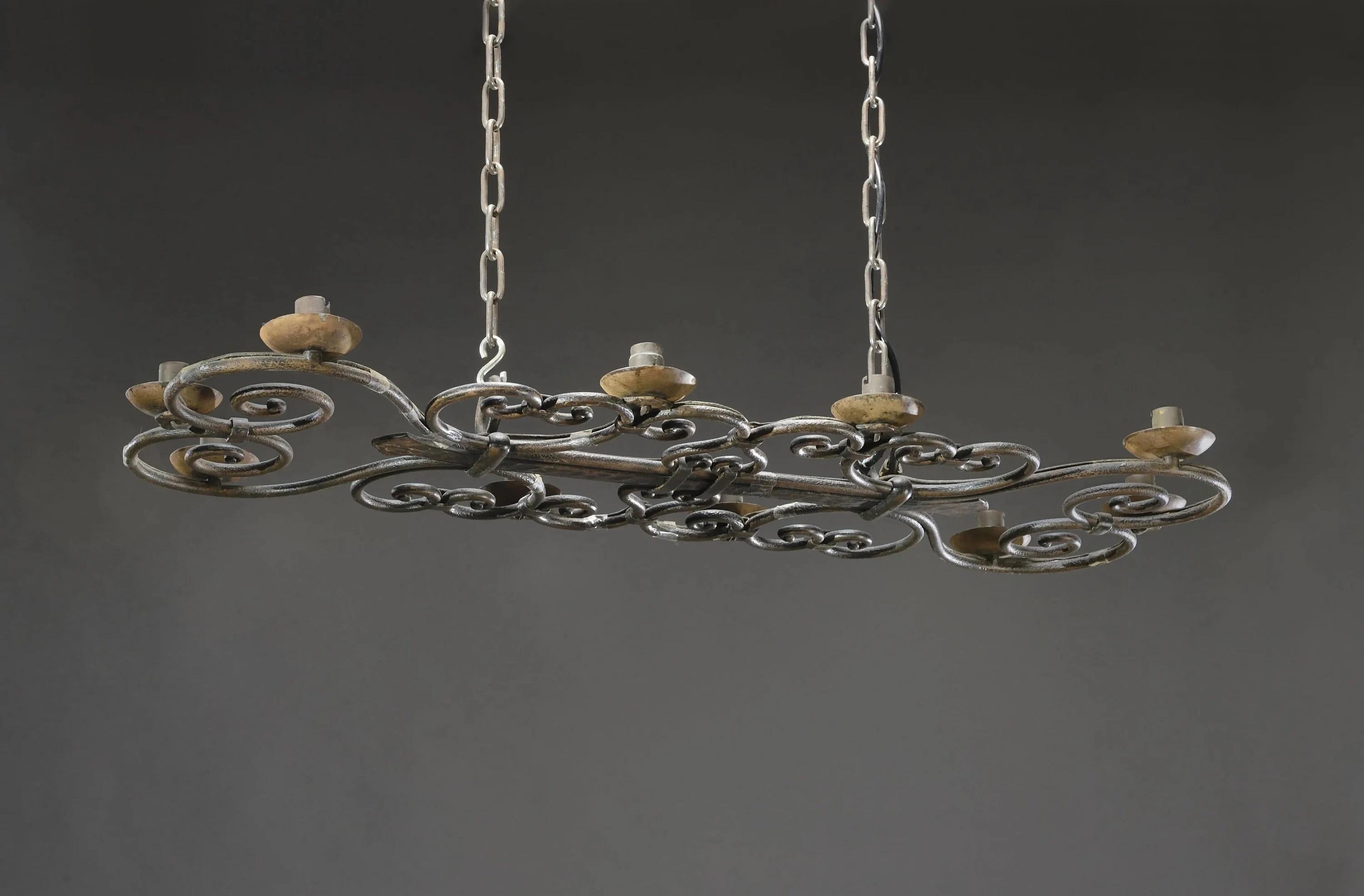 Araña de hierro forjado de Michel ZADOUNAISKY (1903 - 1983), martillado, con nueve brazos. Cuerpo de volutas y entrelazos unidos por un puntal central con decoración de palmetas martilladas con amplias facetas. Cadenas de suspensión regulables en