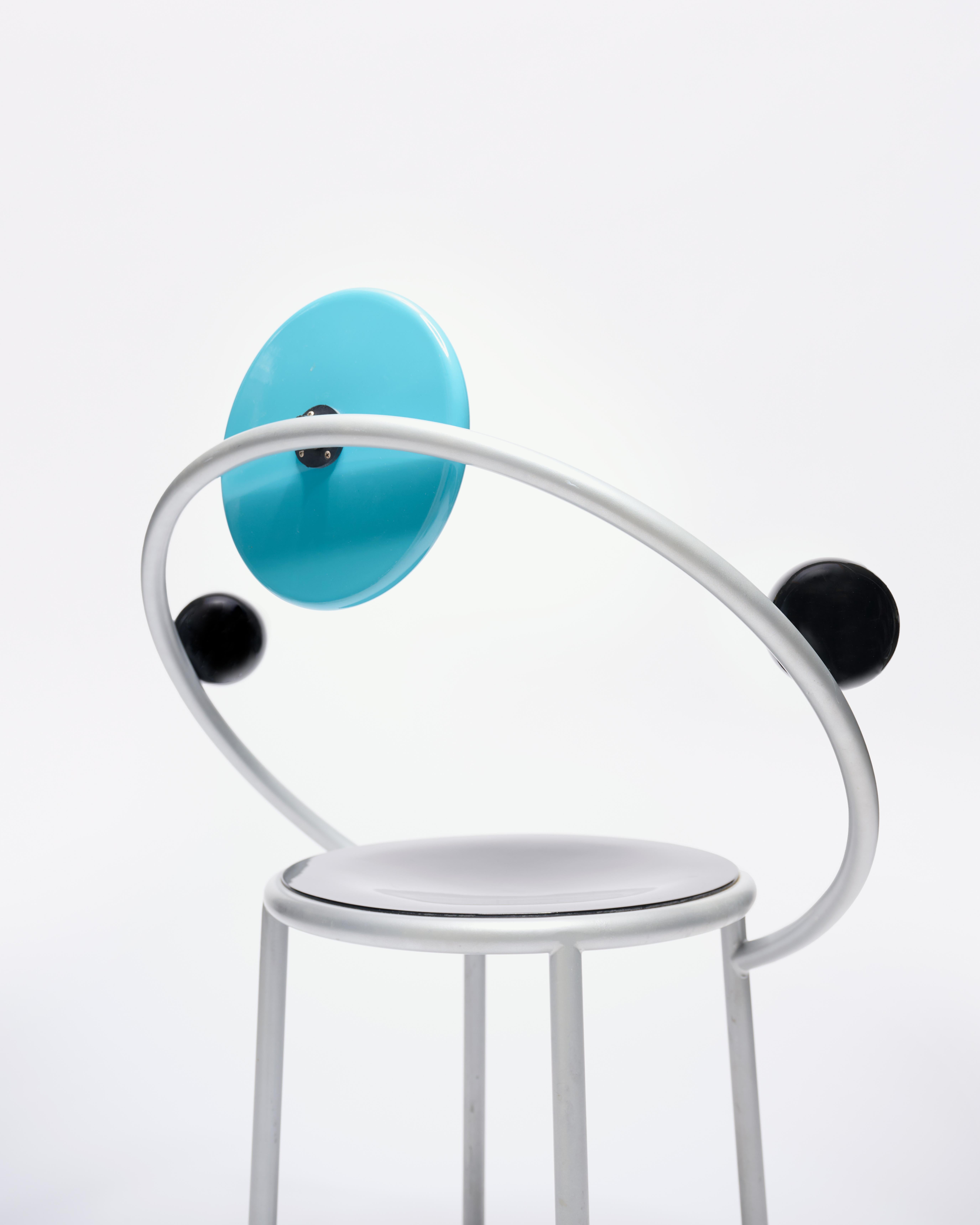 Designed in 1983 by Michele de Lucchi, the ‘First Chair’ is a landmark piece in the Memphis Milano collection as the only original Memphis design to be mass-produced, with an estimated 3,000 units made. 

The chair features a dramatic gray varnished