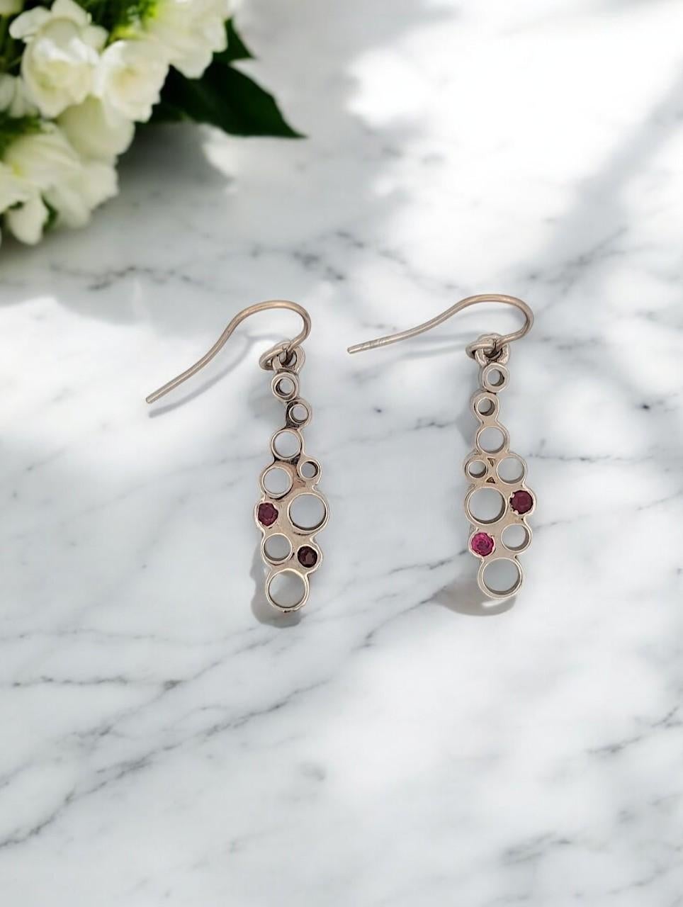 These exquisite handmade earrings by local jeweler Barb Evans are a testament to fine craftsmanship and unique design. Crafted in 14k white gold, they feature open spaces that enhance their modern look and are adorned with natural rubies for a pop