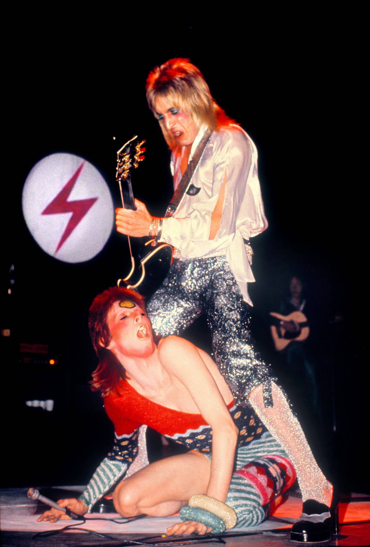 Mick Rock Color Photograph – Mick Ronson, David Bowie im Straddling-Stil, Farbfotografie, Kunstdruck