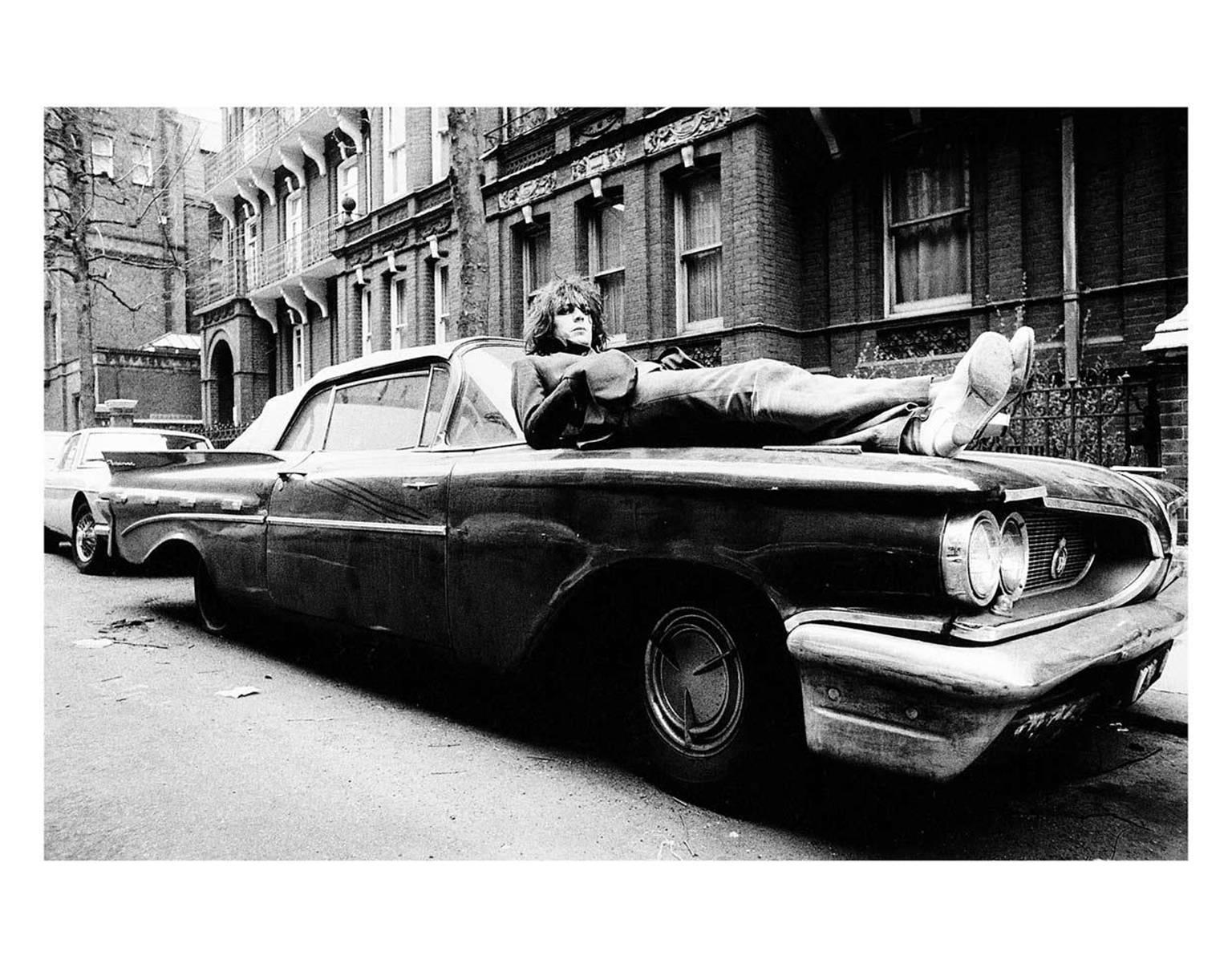 Mick Rock Black and White Photograph – Syd Barrett, Lying On Car, Earls Court Square, London 1969