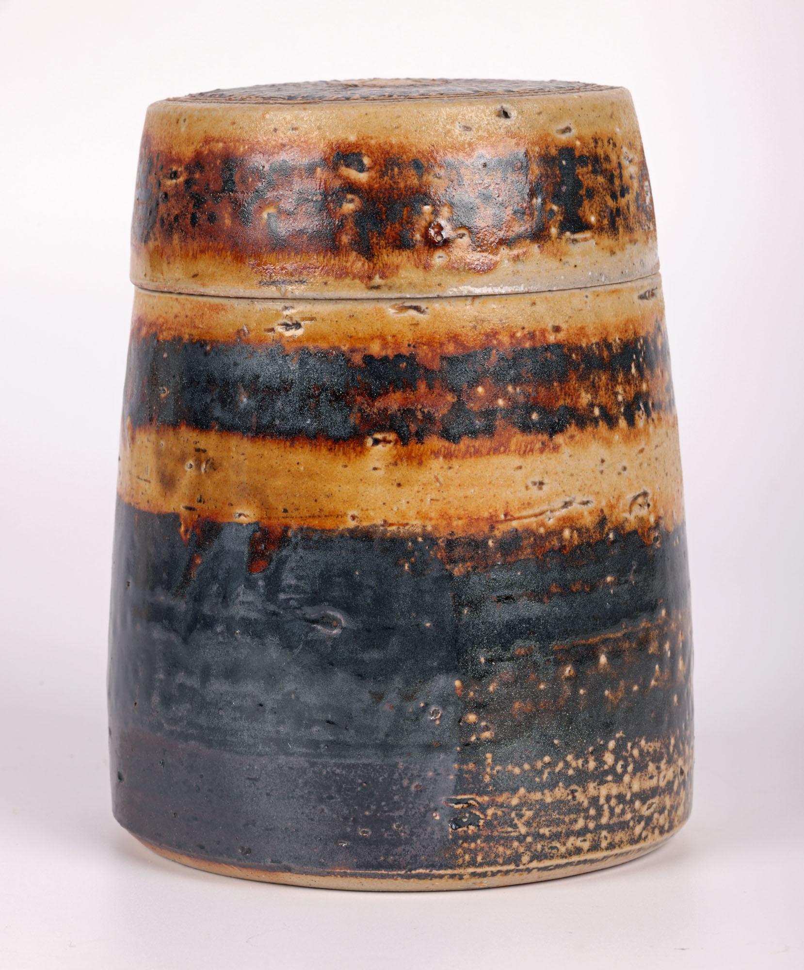 A fine vintage British studio pottery lidded vessel by renowned potter Micki Schloessingk (b. 1949) and made in Swansea, Wales. The stoneware vessel is of tall slightly graduated cylindrical shape with a flat top round cover and is decorated in
