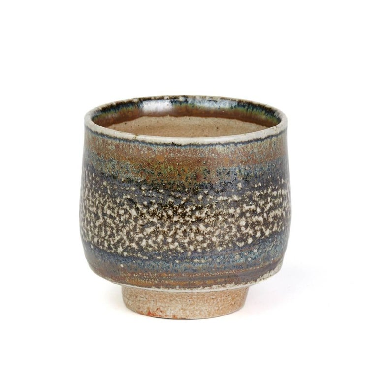 A fine vintage British studio pottery yunomi (teacup) by renowned potter Micki Schloessingk (b. 1949) and made in Swansea, Wales. The stoneware yunomi is of rounded cylindrical shape decorated in metallic blue and green glazes over a stone ground