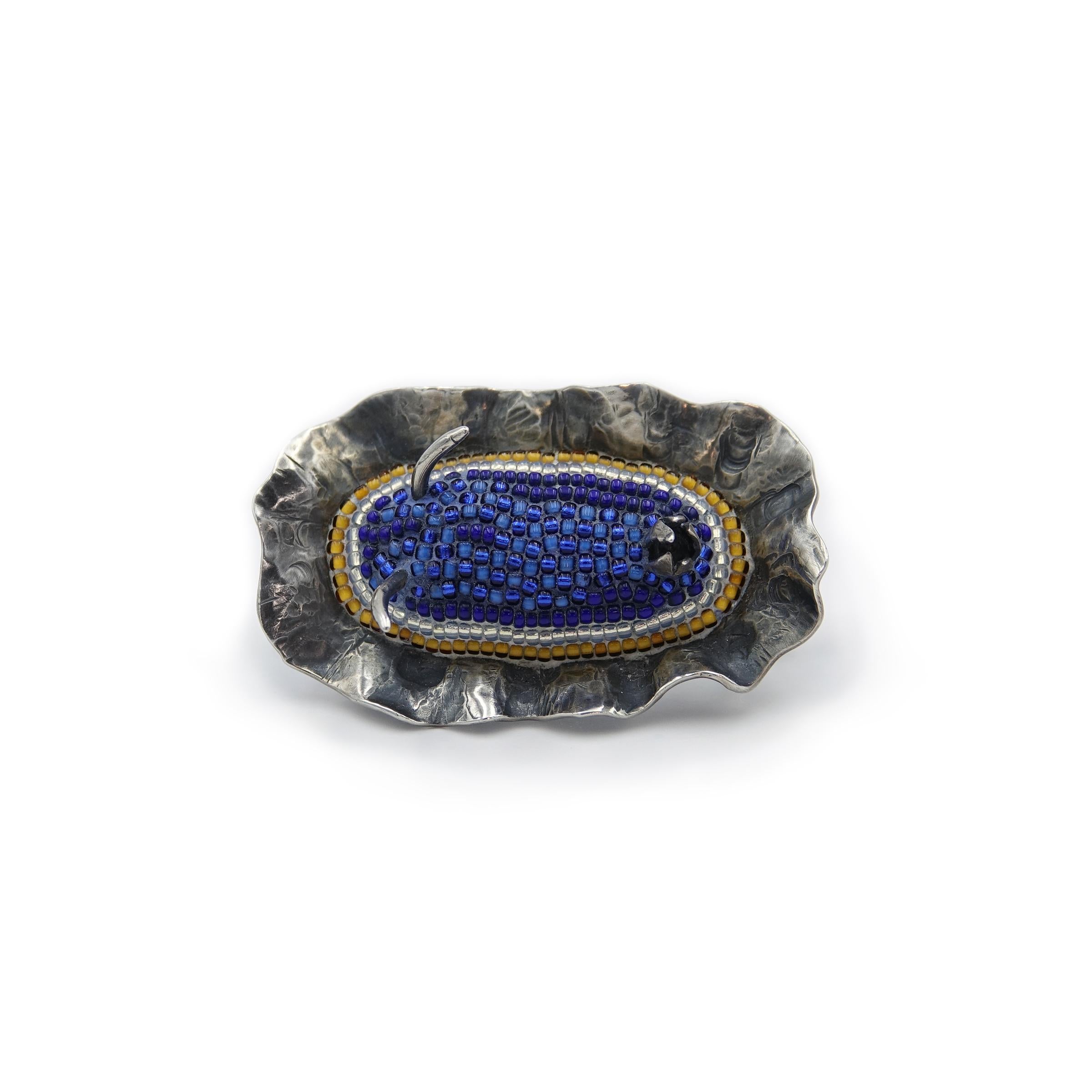 Hand-forged of sterling silver, inlaid with tiny glass seed beads, this micro-mosaic brooch has two tie tack-style pins on the back for versatility and security. 

Part of a body of work created to raise awareness for the world's oceans. Nudibranchs