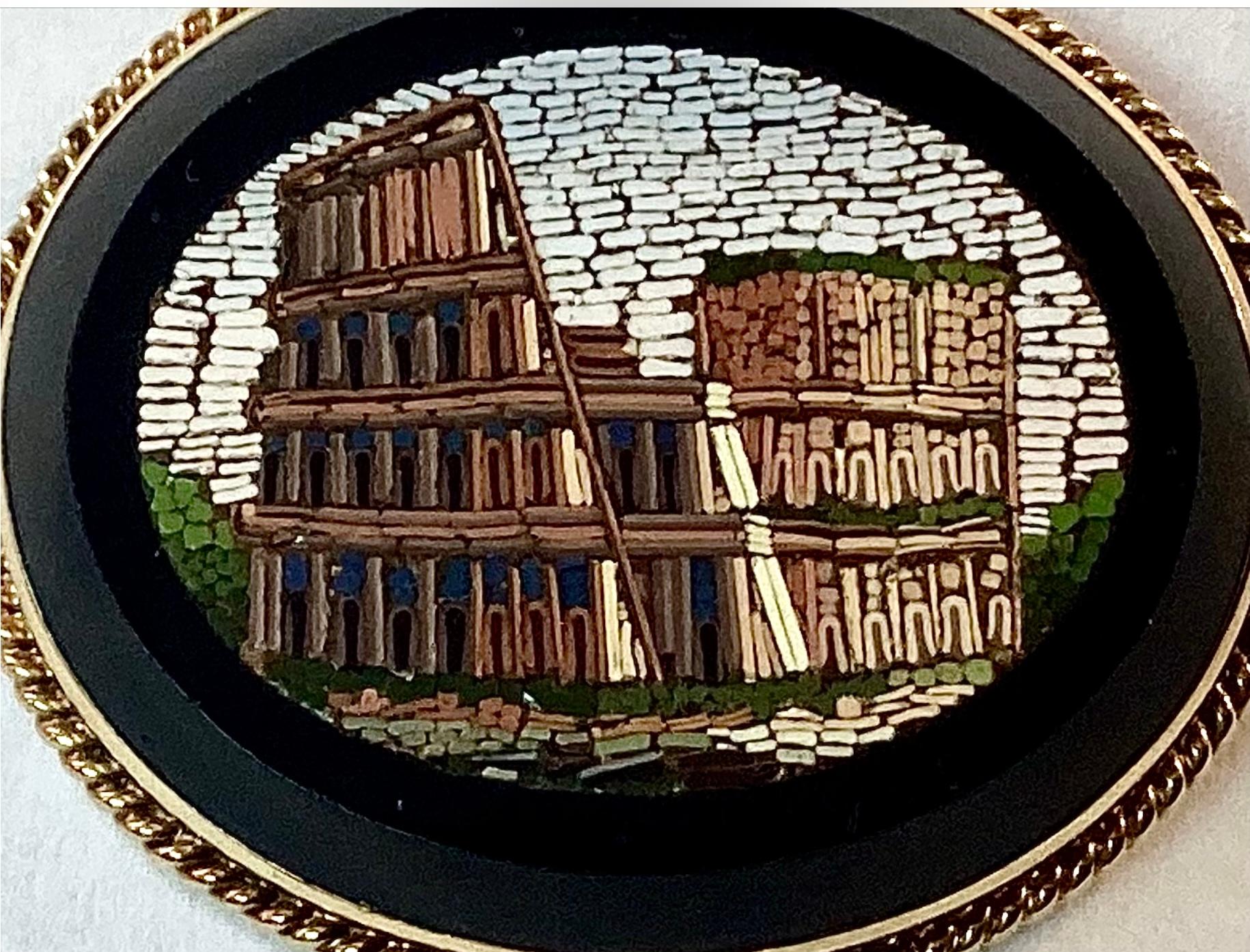 Early 20th century Micro Mosaic Roman Colosseum brooch. Mosaic is surrounded by a yellow gold woven rope frame. Colors include brown bricks, green land and white sky all on a black background. .
