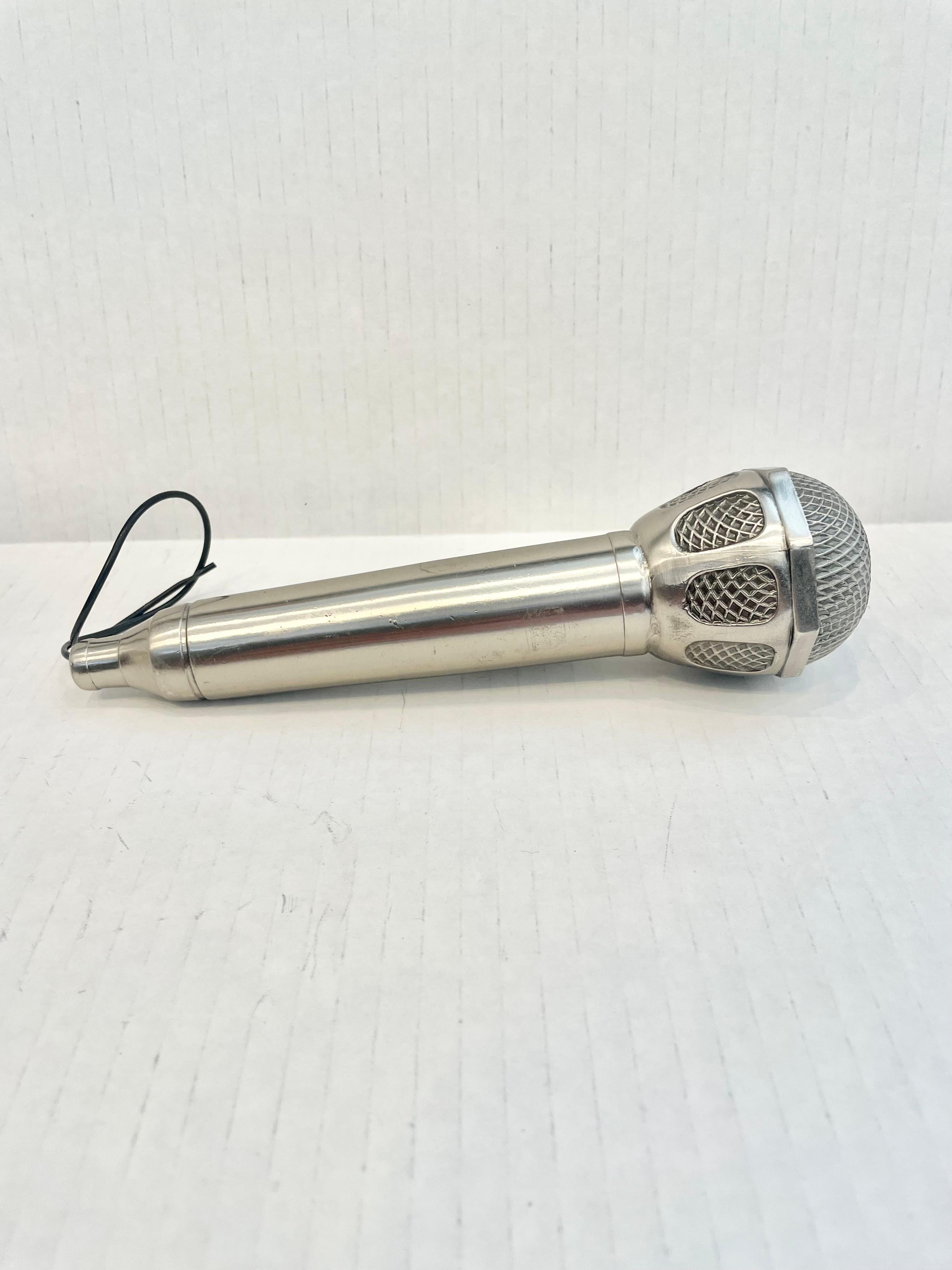 Tolles Vintage-Tischfeuerzeug in Form eines Mikrofons. Etwas über 7 Zoll lang. Vollständig aus Metall mit einem hohlen Körper. Leichte Patina verleiht diesem Stück eine klassische silberne Farbe. Der Kopf hat einen detaillierten Kühlergrill und ein
