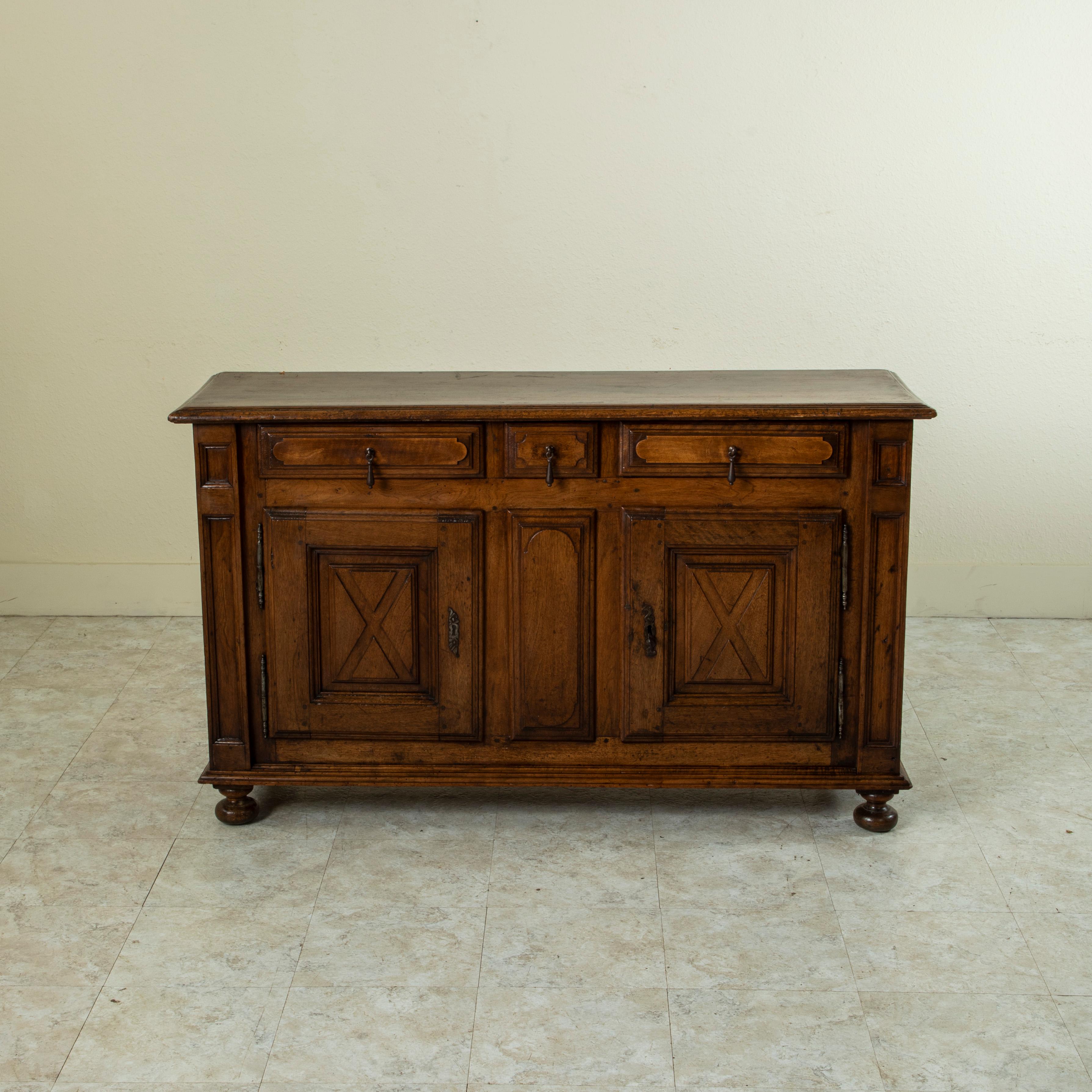 This mid-seventeenth century French Louis XIII period walnut sideboard or buffet features hand pegged construction and solid panels on both front and sides. The buffet has a beveled top made of a single piece of walnut and rests on bun feet. Three