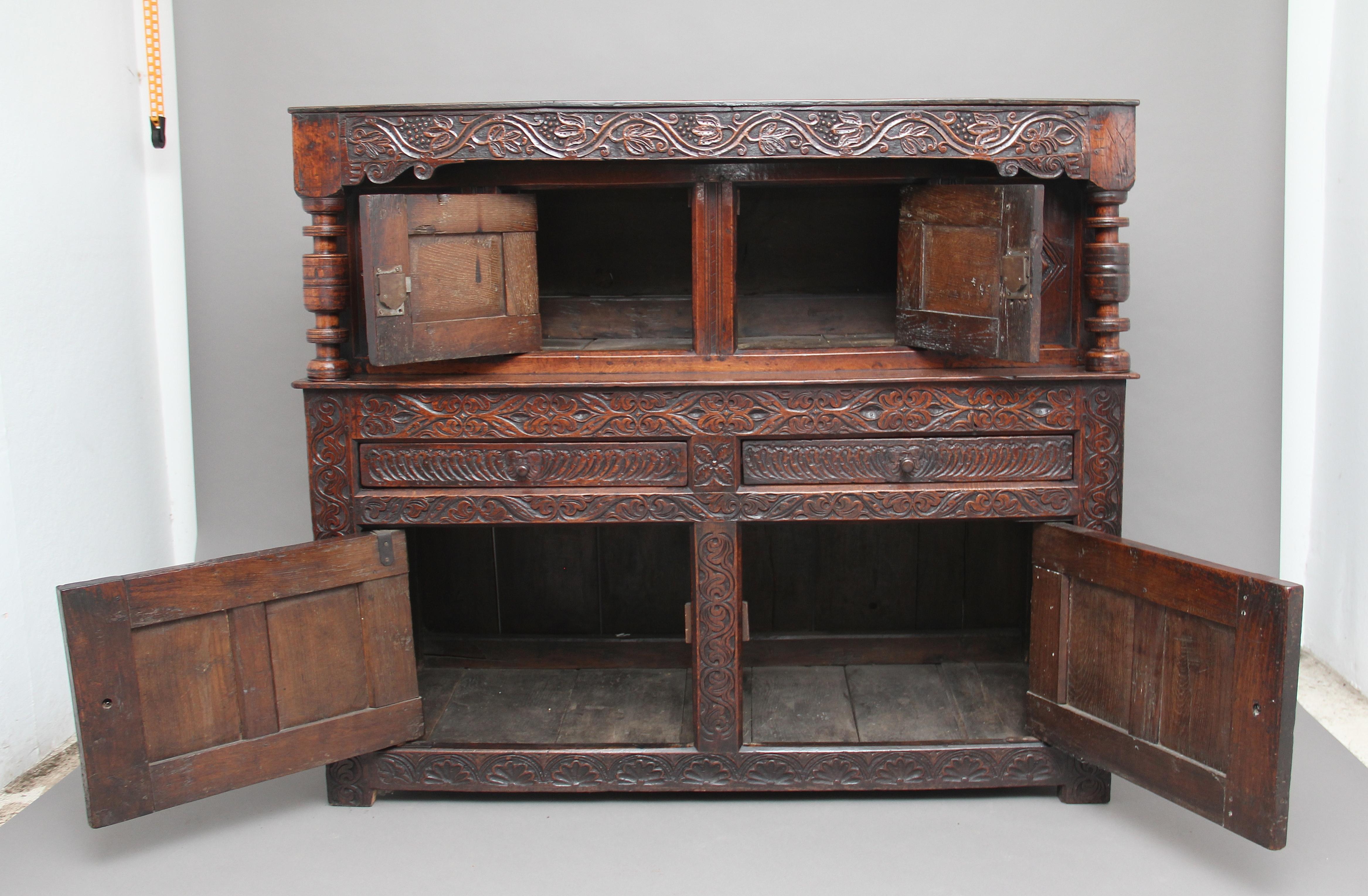 A lovely quality mid-17th century oak court cupboard of good proportions, the cupboard decorated with carved scrolling vines, the frieze over two cupboard doors flanked by turned columns, two oak lined drawers at the centre with lovely carved drawer