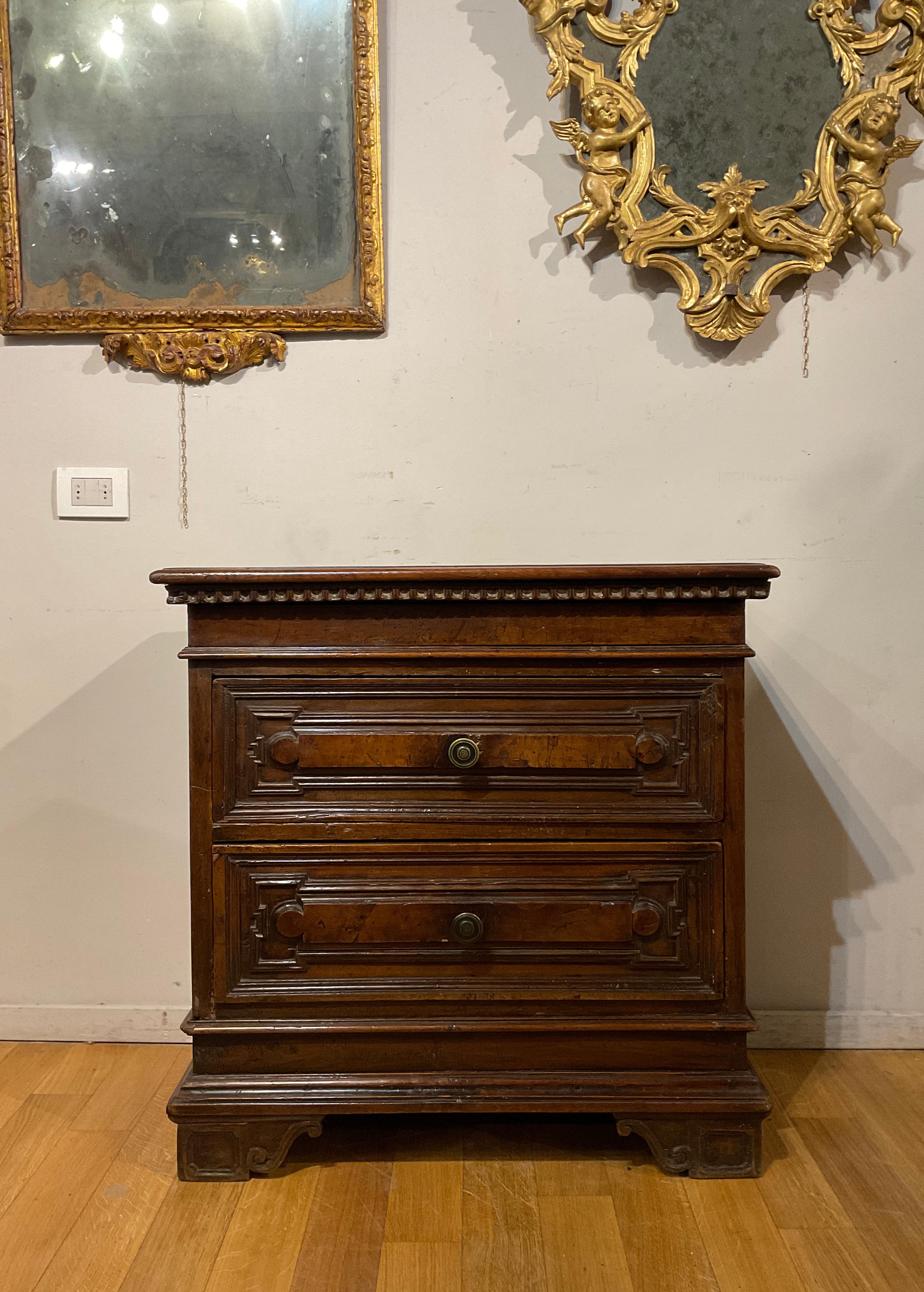 Beautiful walnut chest of drawers with two drawers with bronze knob and a drawer hidden under the top. The drawers are carved to create geometric lozenge motifs, just as under the top the carving recalls classical motifs, characteristics that make