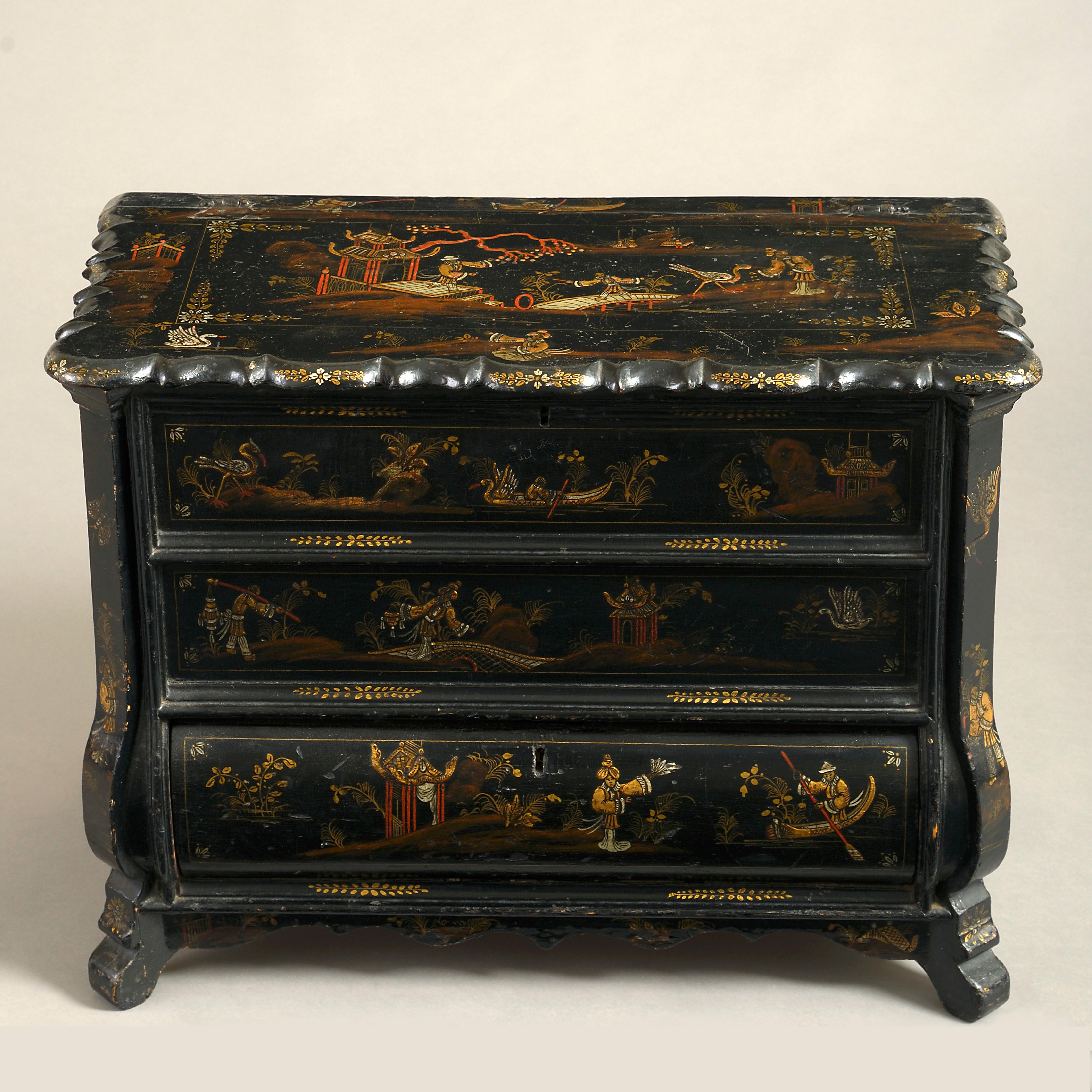 A charming mid-18th century black japanned work box, in the form of a miniature bombé commode, the overhanging shaped top and bottom drawer opening to reveal red painted compartments, decorated throughout with gilded chinoiserie.