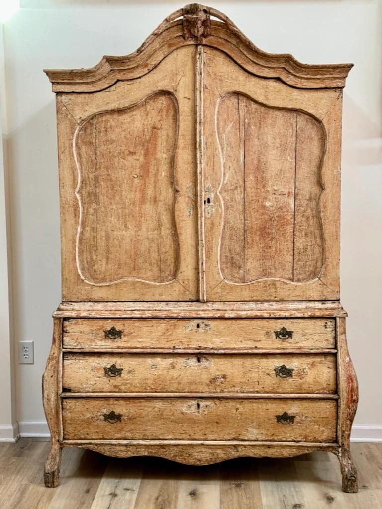 Small mid-18th Century Dutch cabinet on chest, hand-scraped to original paint. Arched pediment with carved foliate and urn crest and finely molded cornice above two wavy top paneled doors. Bombe base comprising three long drawers with figured apron,