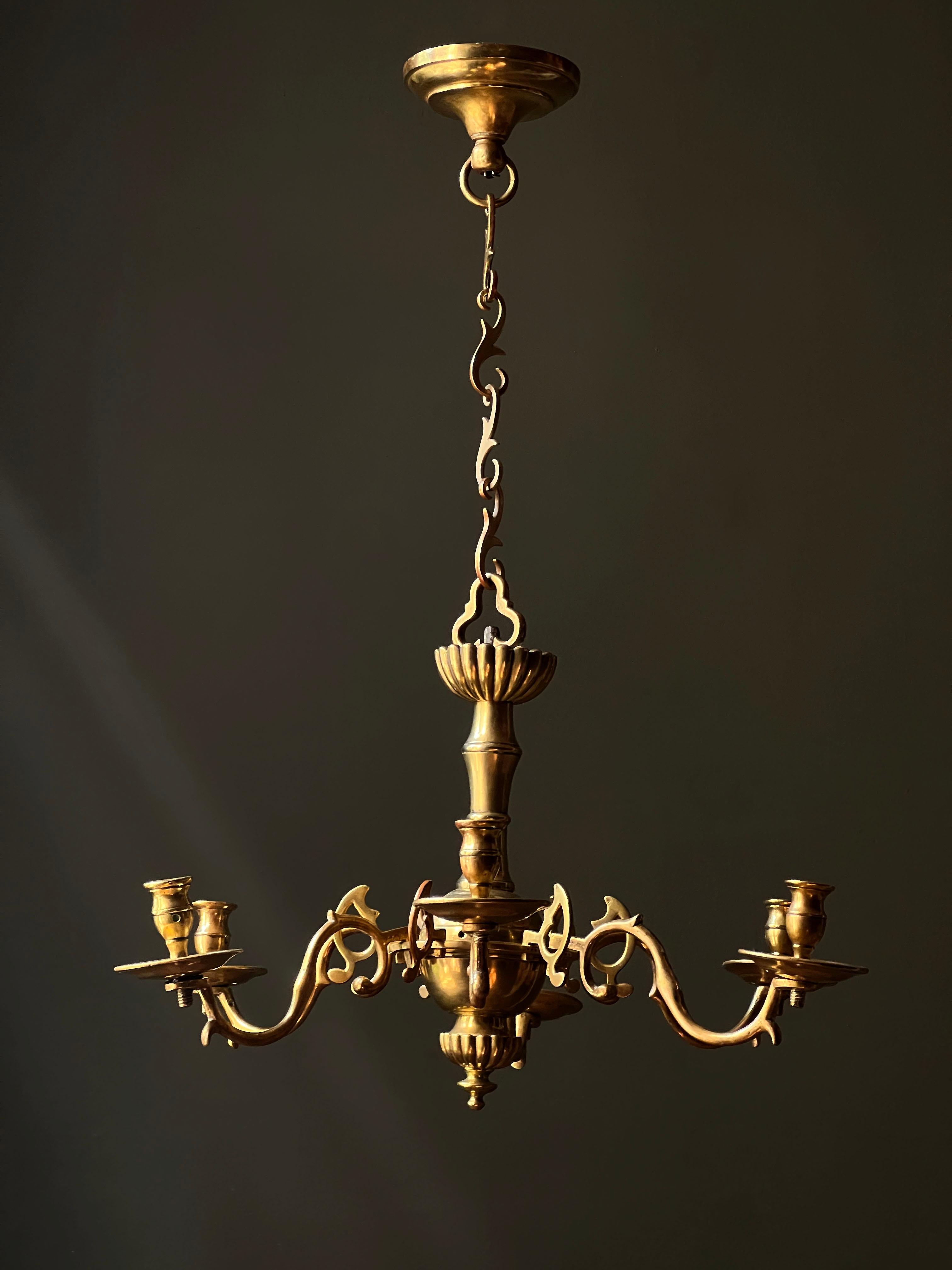 An extraordinary period 18th century brass chandelier of rare form.  Delicate leaf links suspended from the original ceiling mount support a trefoil hook and the body of the light from which extend six branch arms and bobeches with alternating