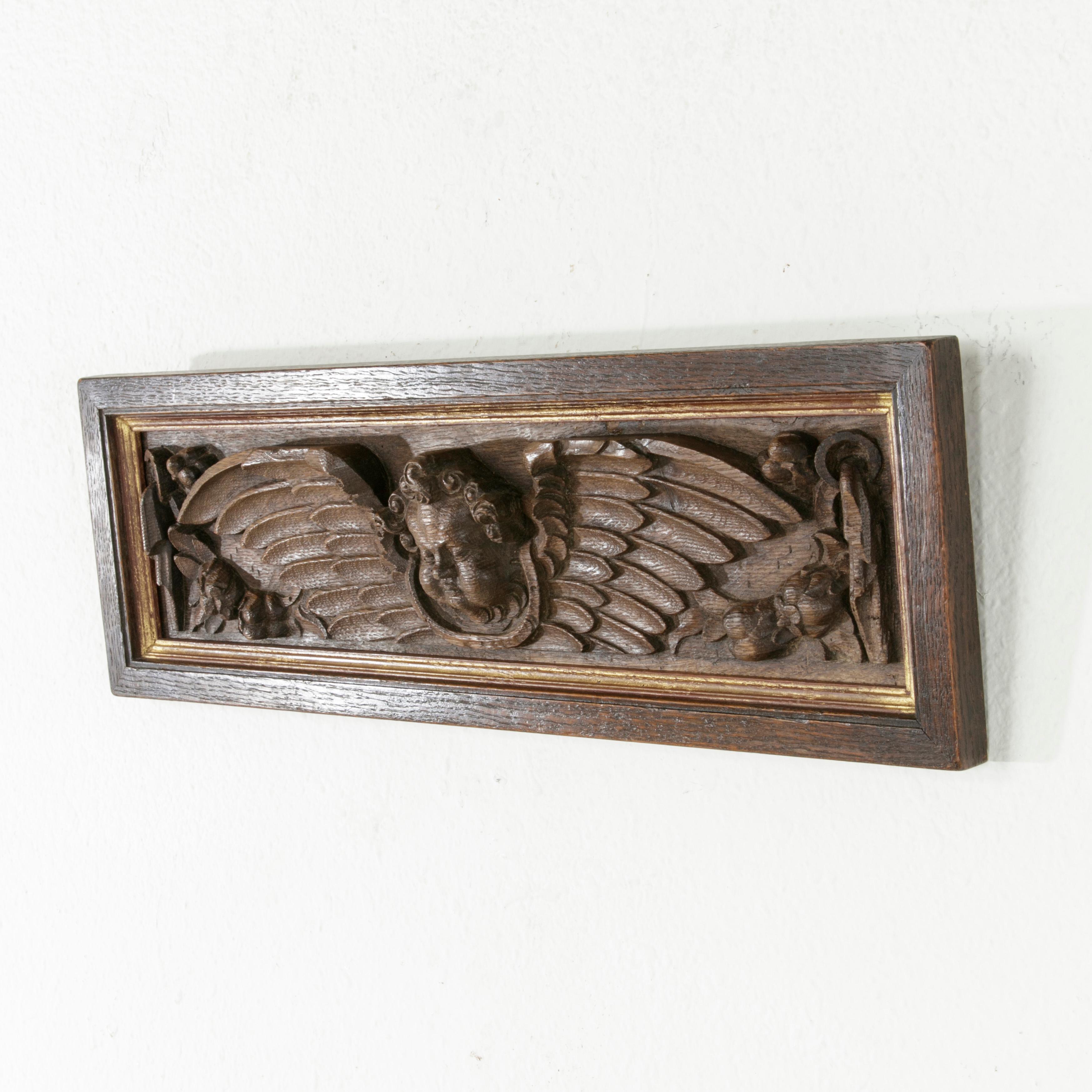 This French deep relief hand carved oak panel from the mid-18th century features an angel's face flanked by wings. Additional carvings of garlands of flowers draped from rings detail the piece. The Louis XV period panel is surrounded by an oak frame
