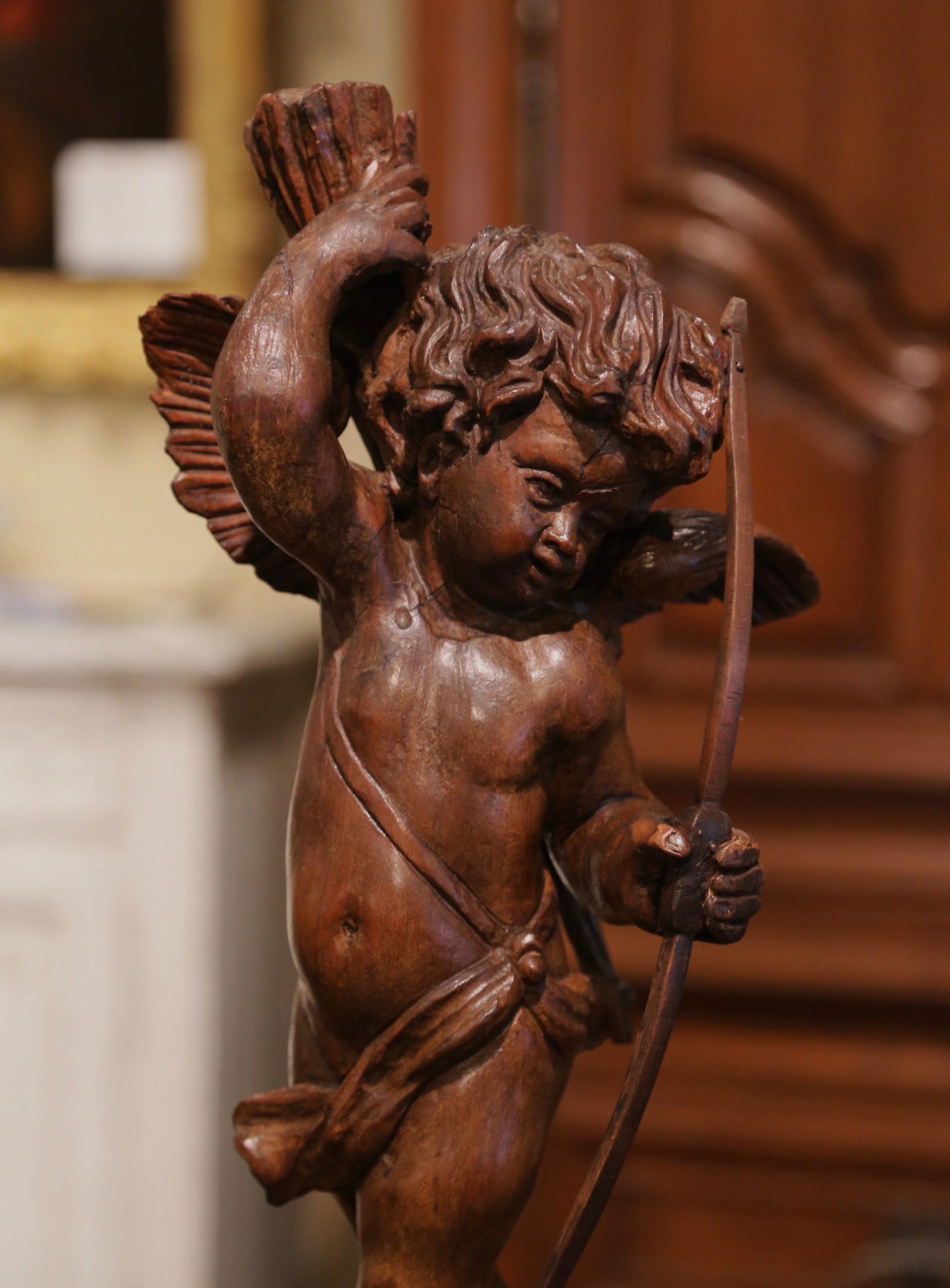 This elegant antique putti figure was carved in France, circa 1750. Standing on a double square base, the detailed statue features a young boy with wings holding a bow in his left hand and reaching for an arrow in his right hand. The adorable cherub