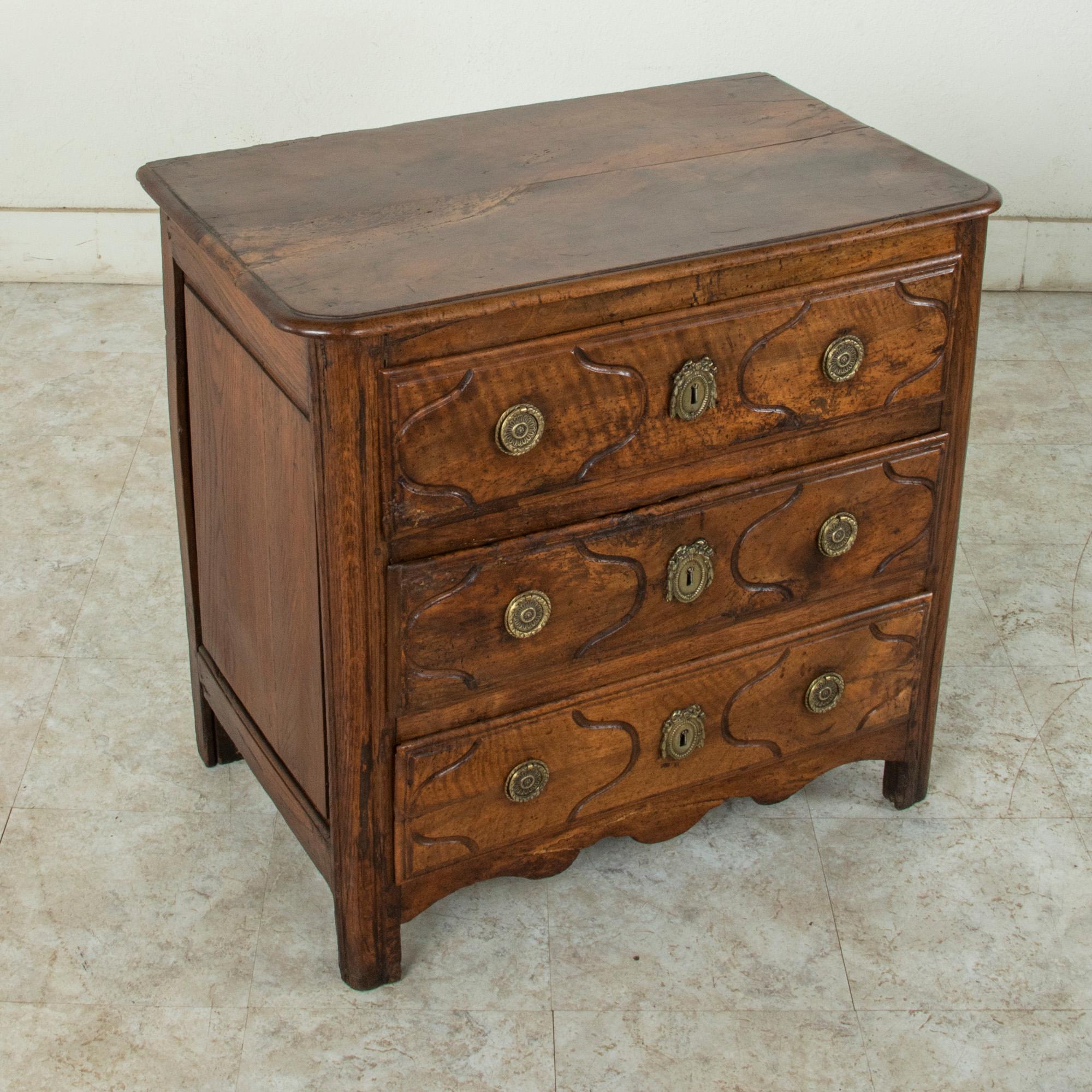 Of an unusual small scale, this 18th century French Louis XIV period commode or chest is constructed of solid hand carved walnut with paneled sides and beveled top. Originally created for a Paris apartment in the Ile de France region, this piece