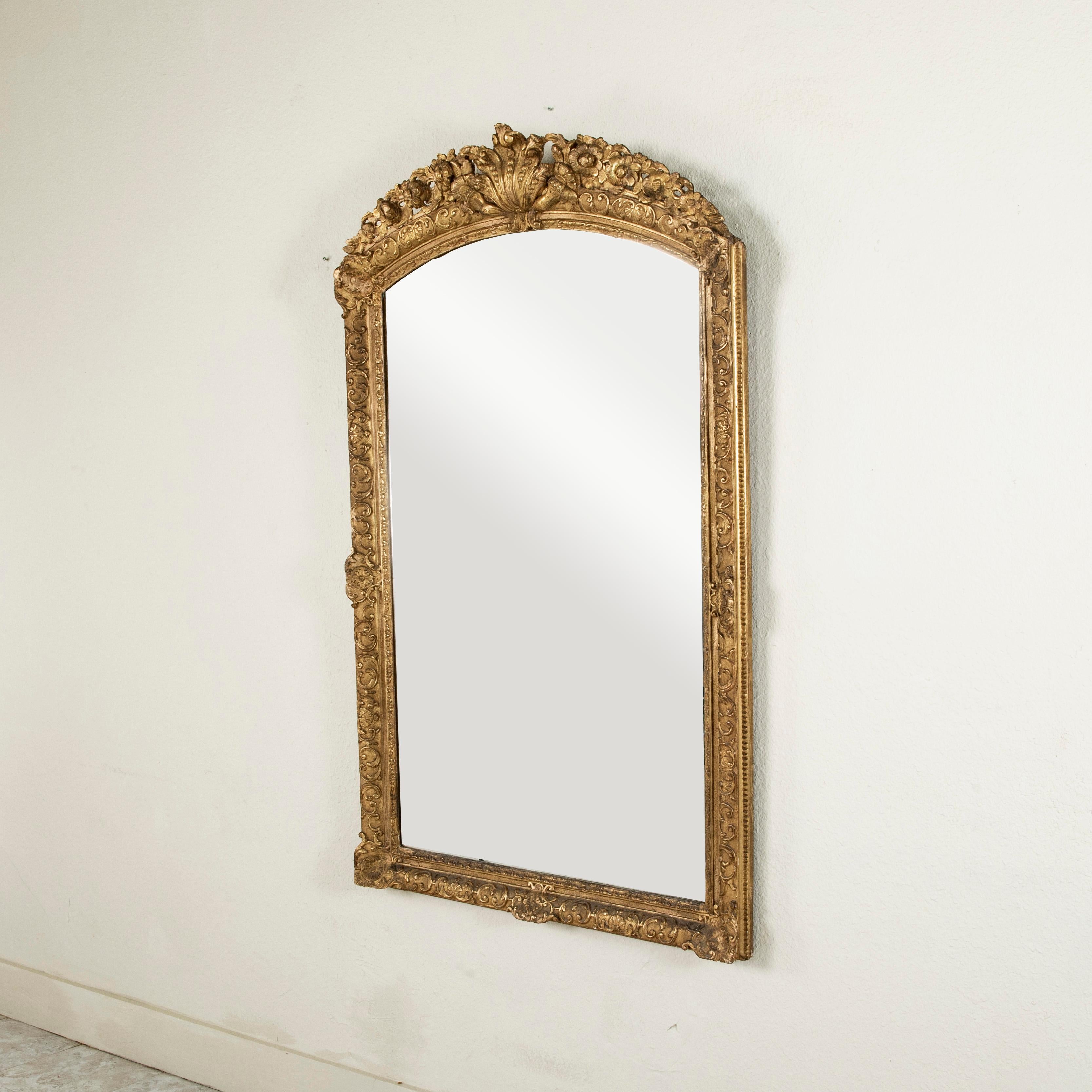 This mid eighteenth century French Regency period gilt wood mirror features a hand carved frame detailed with a central scalloped shell at the top, scrolling leaves and flowers. Shells and acanthus leaves detail each corner. Measuring 60 inches in