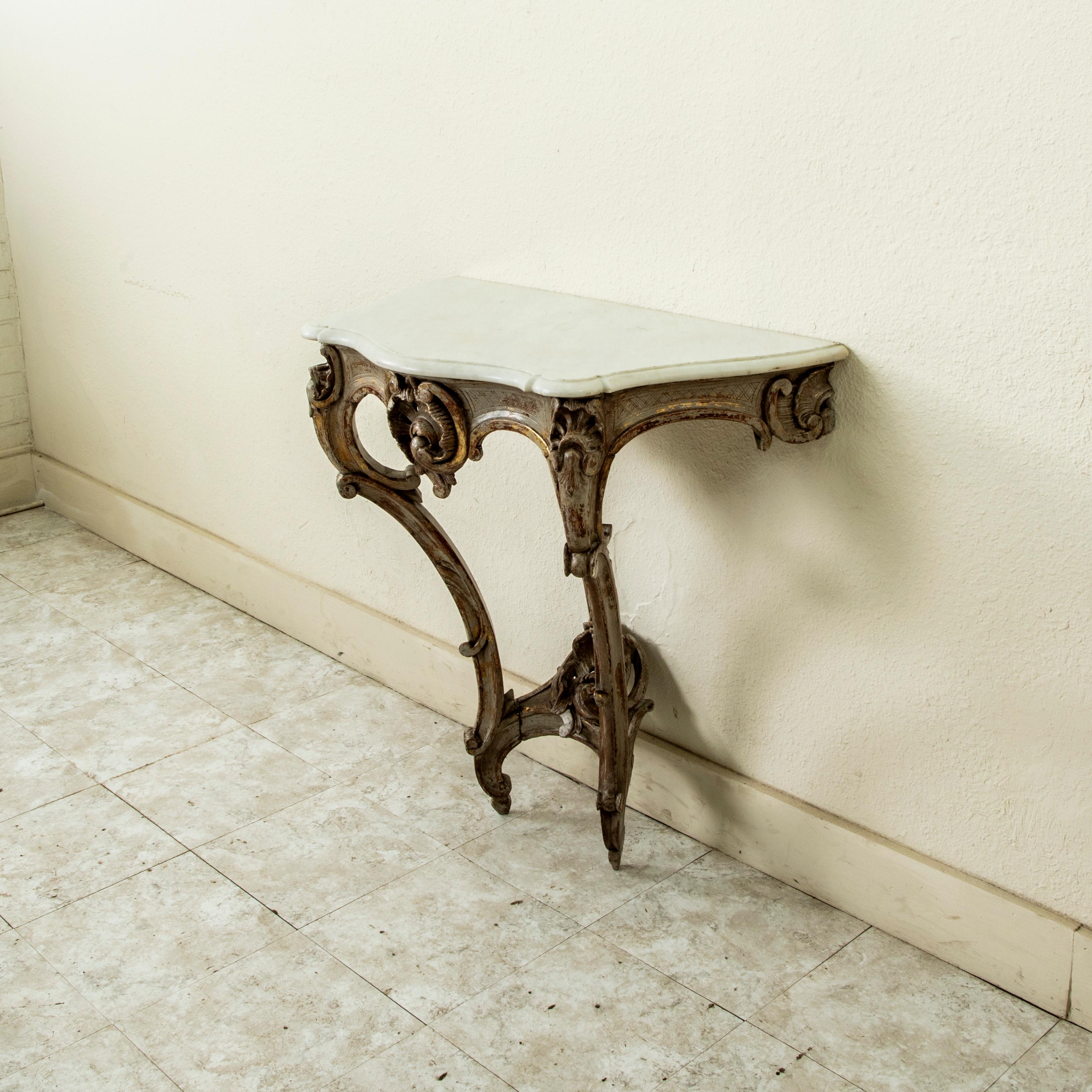 This mid eighteenth century French Regency period wall console table features a beveled white marble with curved front. The hand carved apron below the marble is detailed with a central asymmetrical scalloped shell flanked by C scrolls. Scalloped