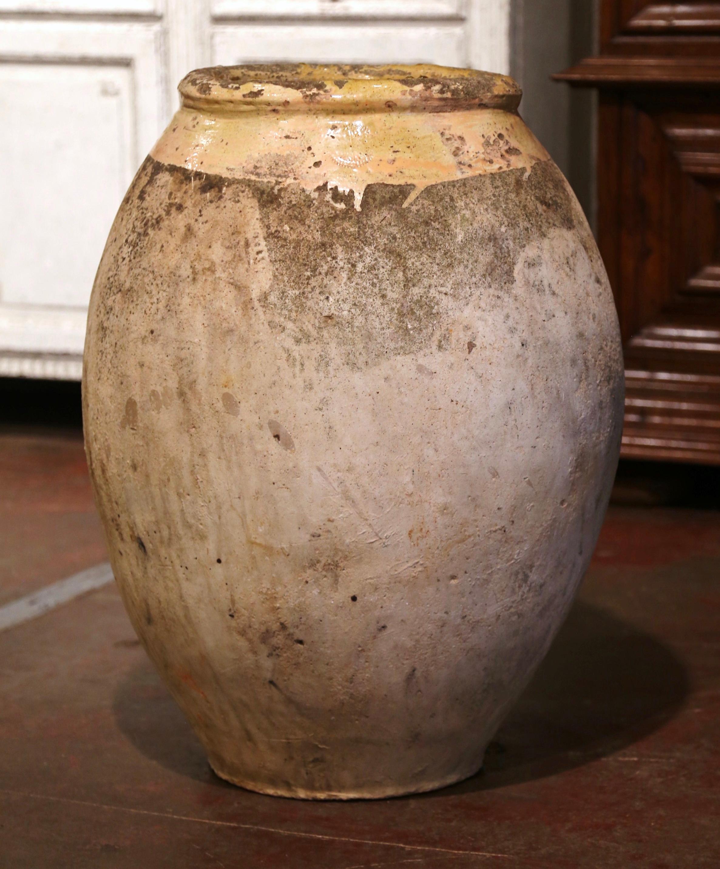 This large, antique earthenware olive jar was created in Southern France, circa 1760. Made of blond clay and neutral in color, the terracotta vase has a traditional round shape. The rustic, time-worn pot features a yellow glaze around the neck and