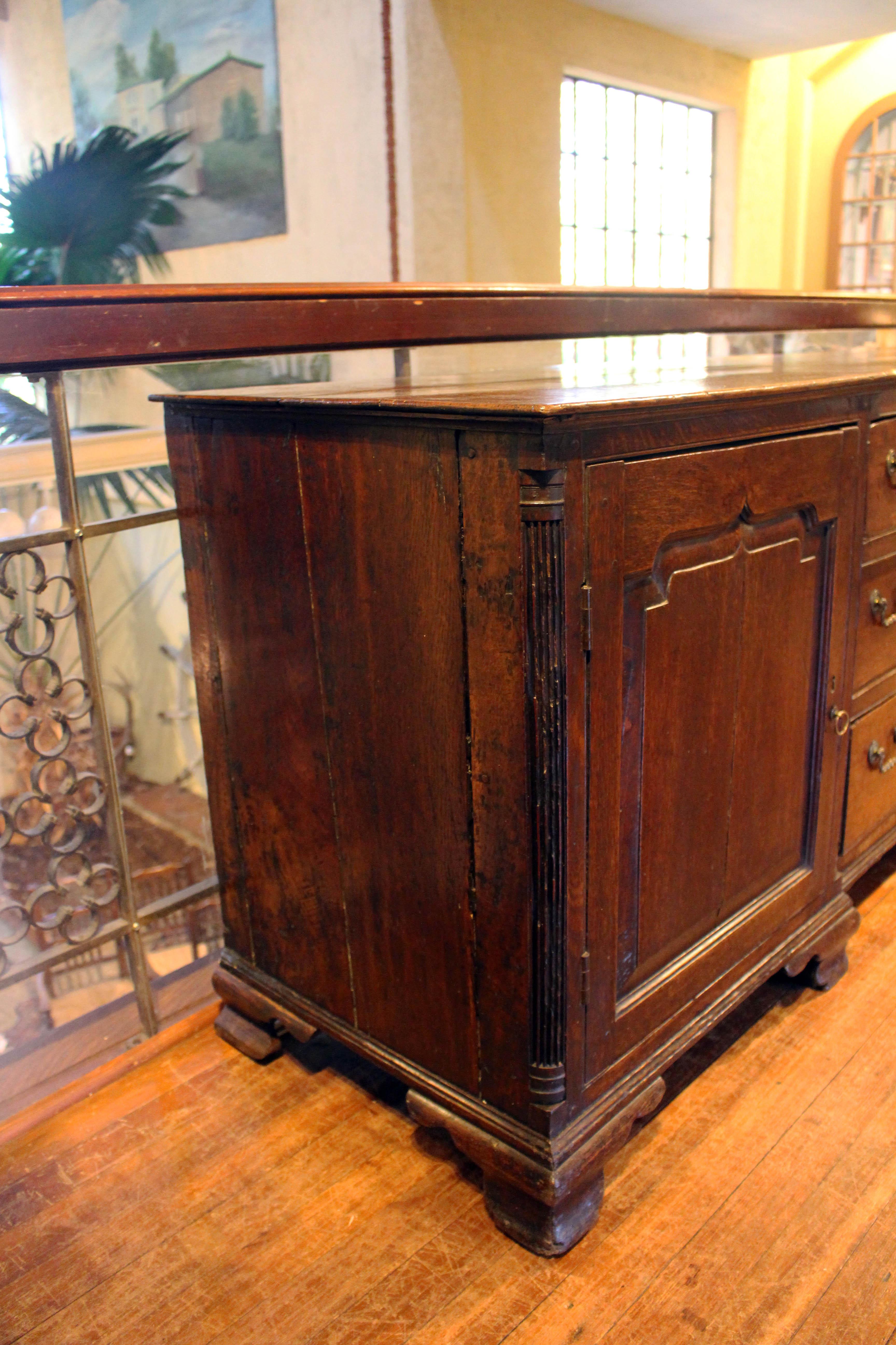 Mid-18th century Georgian dresser base, English, breakfront form. Wonderful mellow oak. Drapery fold panel effect carved doors reflect the influence of earlier design, well molded. Four reeded quarter column corners, flanking the two end cabinets,