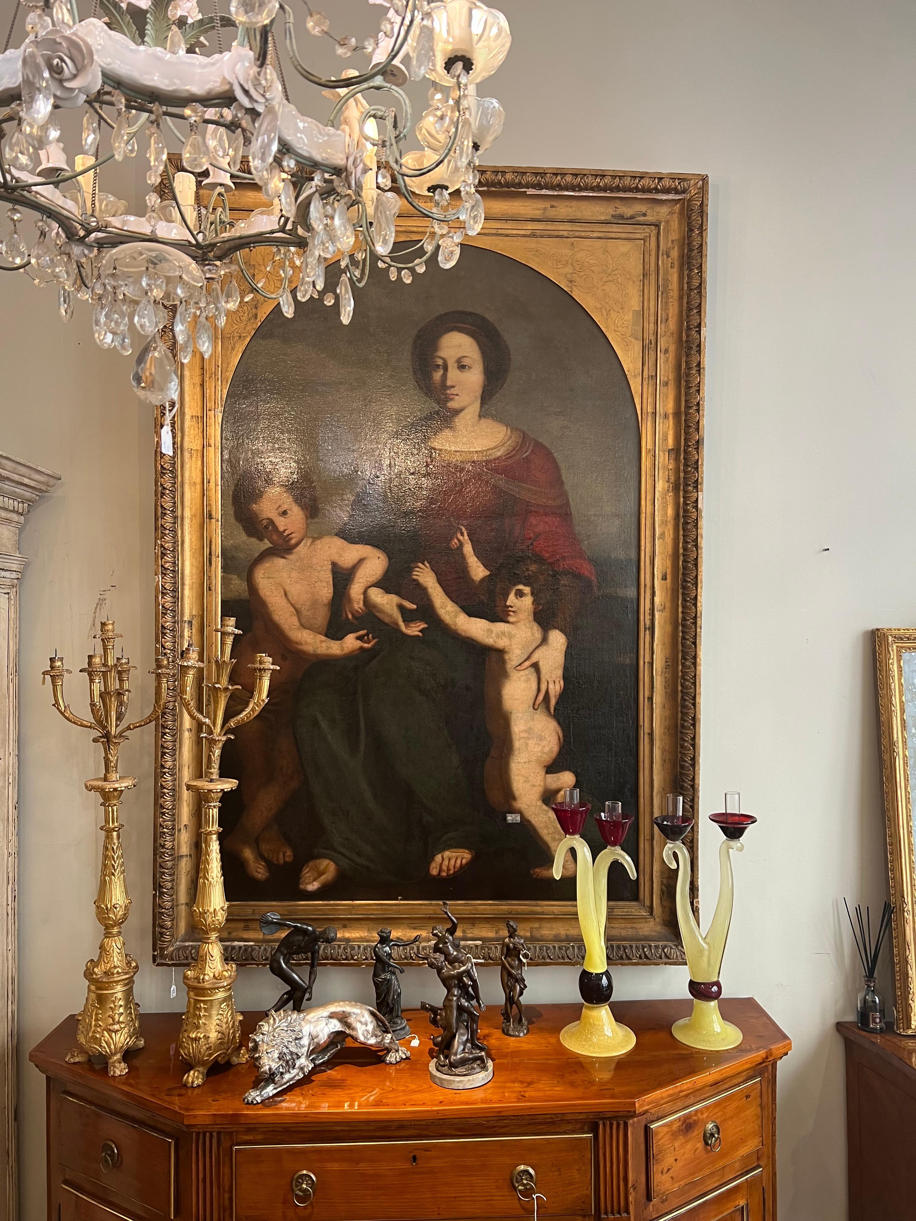 Grande peinture à l'huile sur toile représentant la Vierge à l'enfant et San Giovannino dans un cadre en bois sculpté et doré.
Le sujet est particulier car il sort des canons classiques de la représentation de la Maternité en présentant une Madone