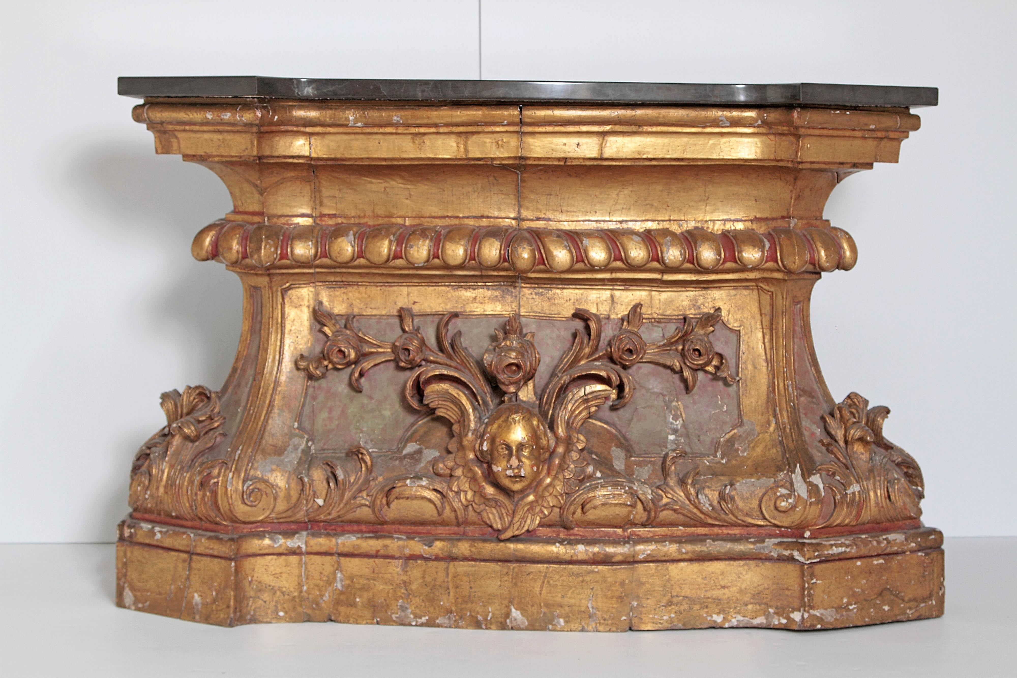 A large mid-18th century Italian gilded and poly-chromed architectural fragment used as a console with later black marble top, shaped base and top, angel face with floral spray on centre of base, mid-18th century, Italy.