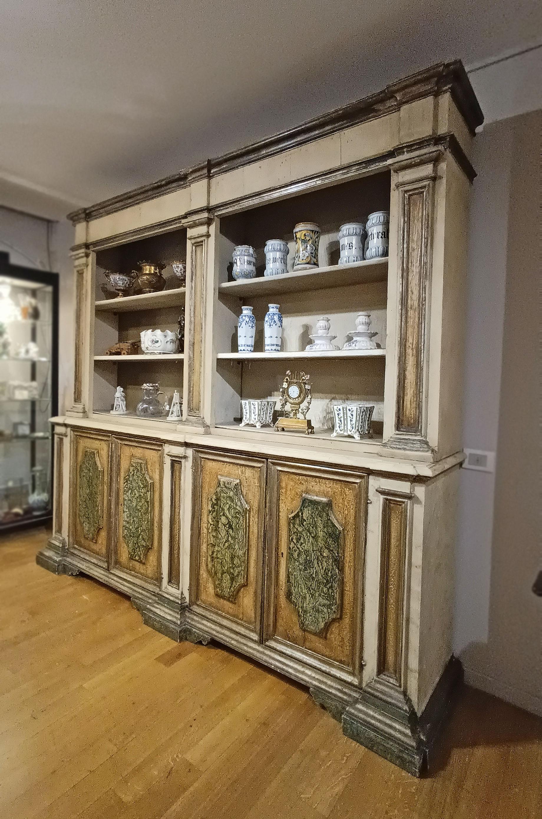 Beautiful large bookcase, crafted from painted fir wood. The bookcase features a double body, with the lower section composed of four doors and the upper section featuring three shelves on each side, ideal for displaying and storing objects. The