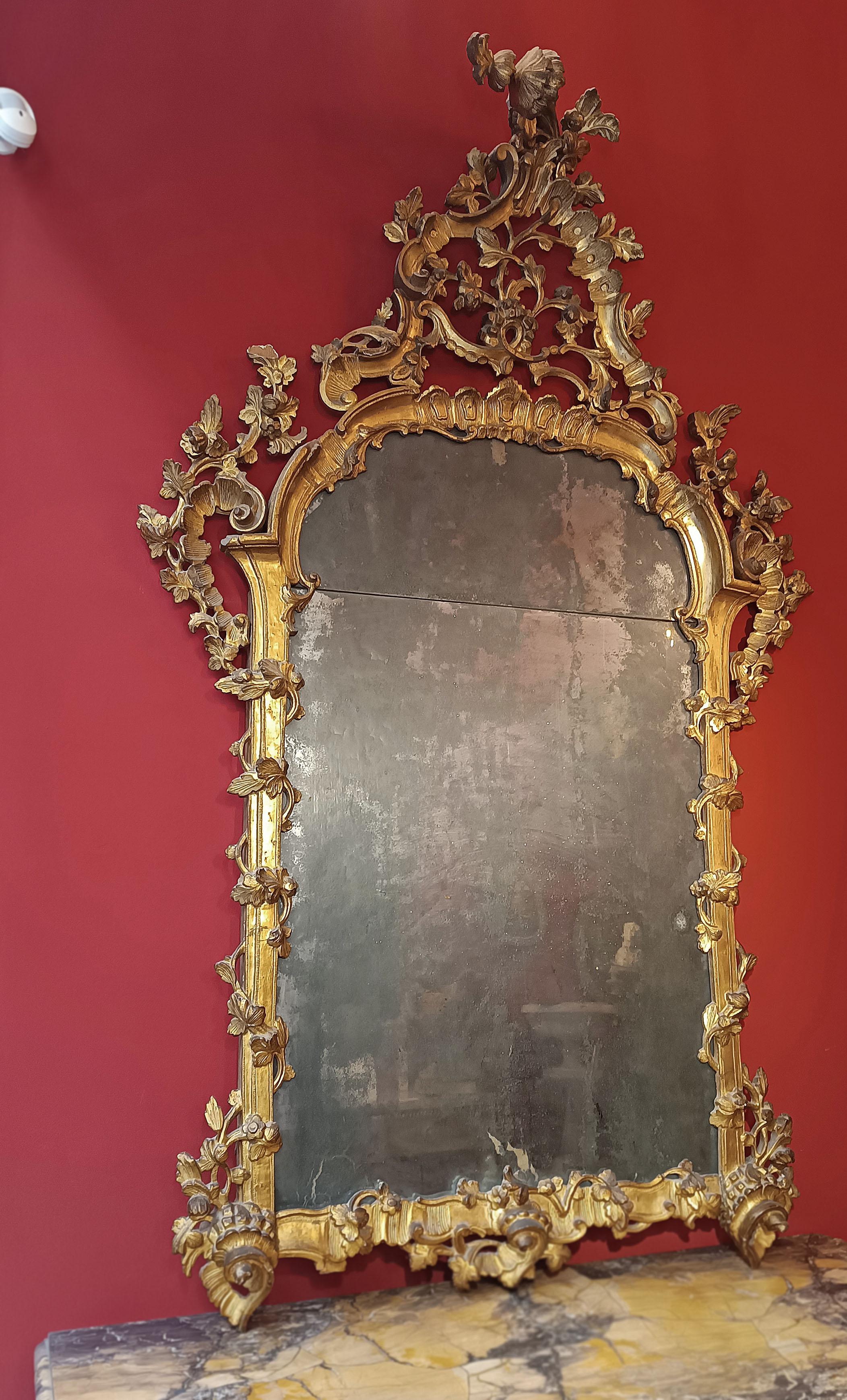 Miroir raffiné en pin suisse sculpté et doré à la feuille d'or pur. Il présente de somptueuses volutes avec des tourbillons et des tresses végétales, dans un style Louis XV parfait, menant à une grande corniche ornée d'encore plus de feuilles, de
