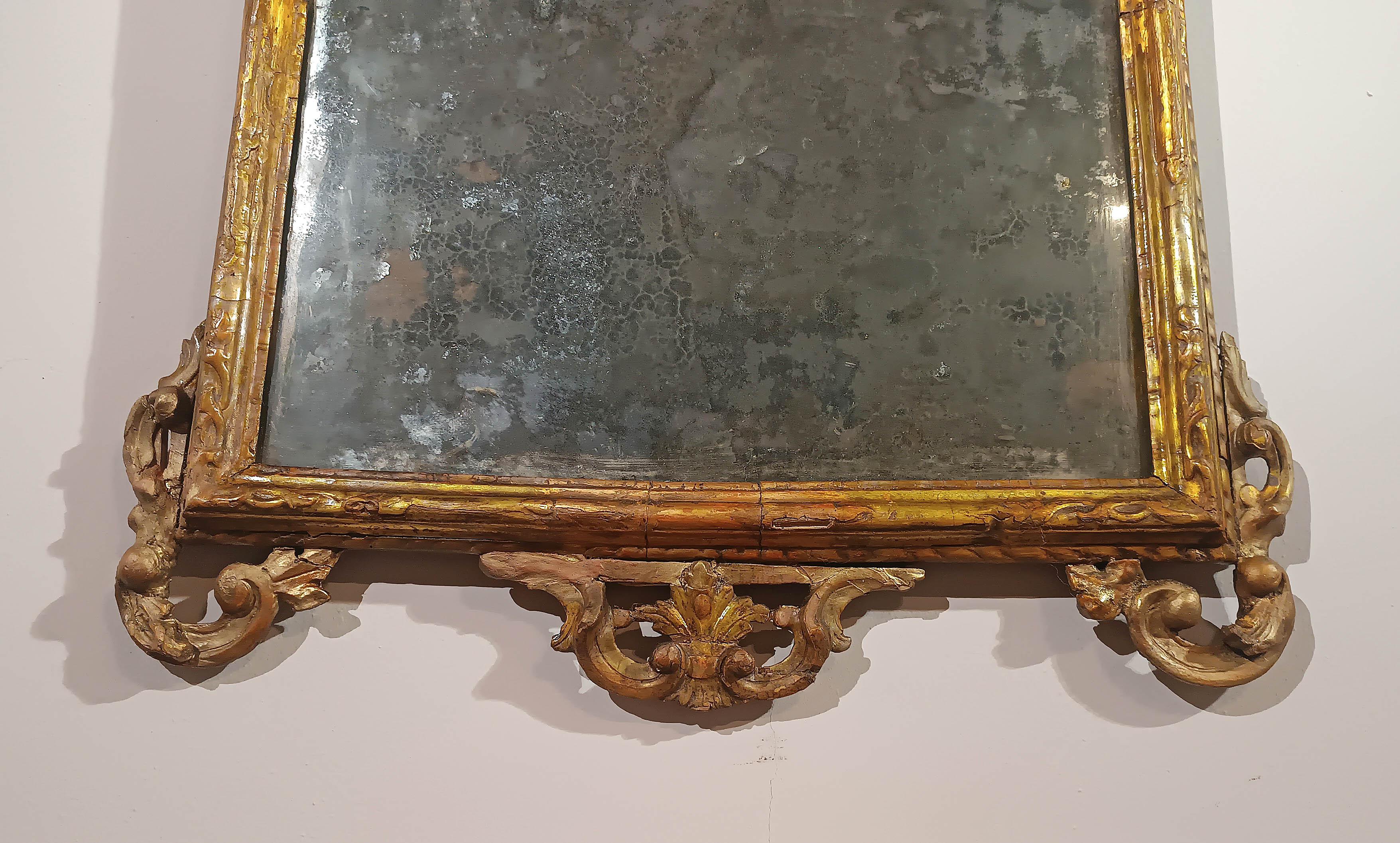 Cet élégant miroir compact est fabriqué en bois de pin suisse sculpté, partiellement doré à la feuille d'or pur et partiellement avec une mecca argentée. Le cadre du miroir est décoré de motifs de rinceaux végétaux sur les parties inférieure et