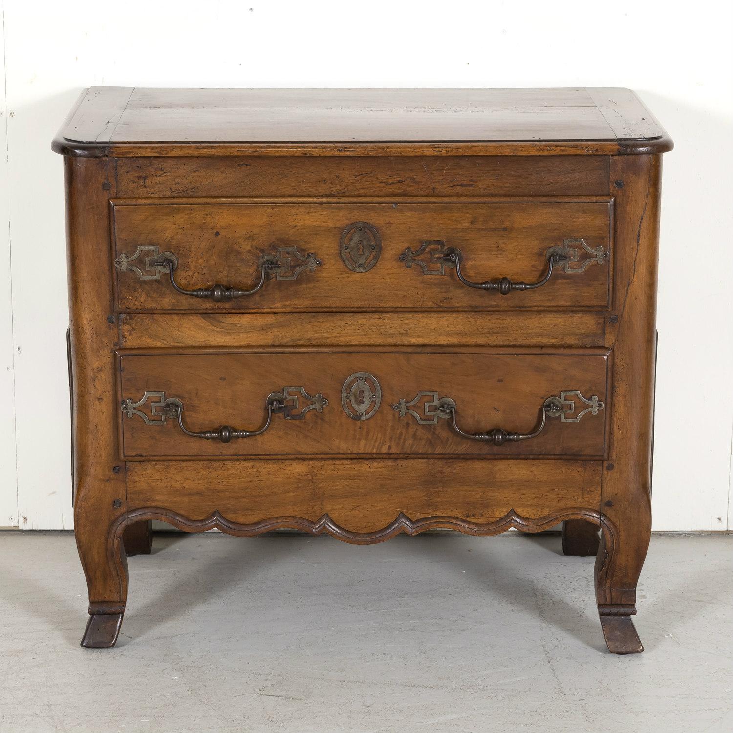 A fine mid-18th century Louis XV period petite commode handcrafted by talented artisans in Bordeaux of solid old growth walnut, circa 1750s, having a beveled edge plank top above two drawers with original iron handles and escutcheons. Carved,