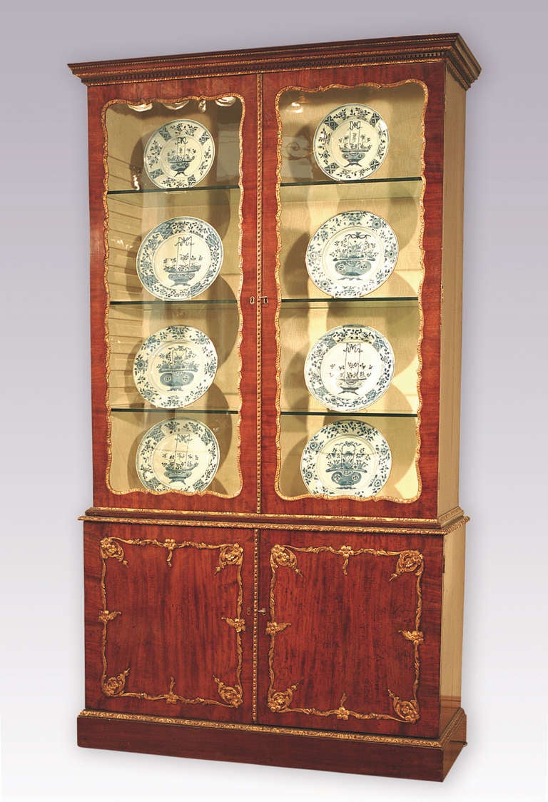 An attractive mid-18th century figured mahogany display bookcase with gilt gesso mouldings throughout having dentil moulded cornice above shaped glazed doors and paneled cupboard doors below, enclosing drawers with original swan-neck handles. The