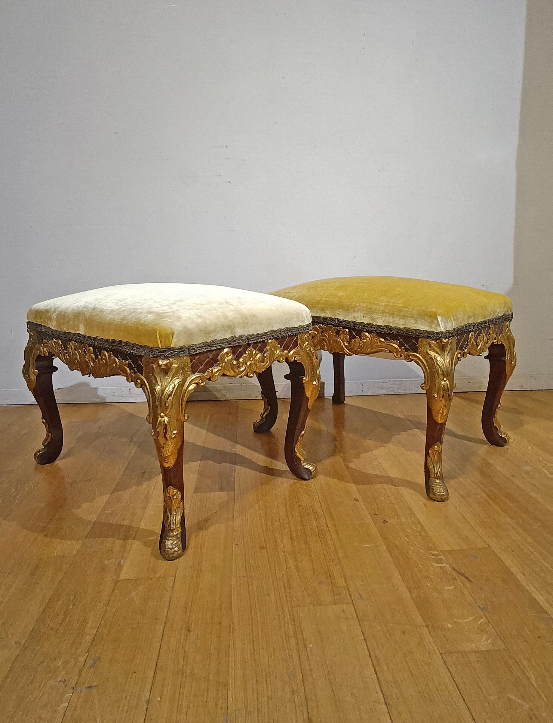 Elegant pair of center stools made of solid carved walnut, embellished with gilded finishes. The latter, characterized by delicate vegetal scrolls, give a touch of further elegance to the stools. They also have wavy legs and a seat covered in