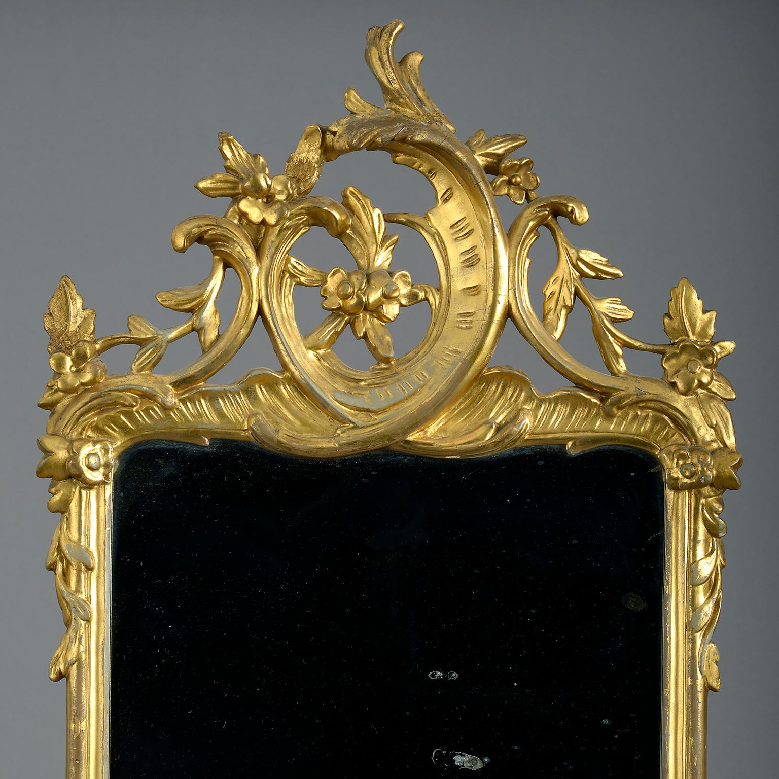 Mid-18th century giltwood mirror, the rectangular mercury-silvered plate contained within a frame of bold rococo scrolls and foliate swags in the manner of Johann Michael Hoppenhaupt.

The richly carved frame of rocailles and C-scrolls and sinuous