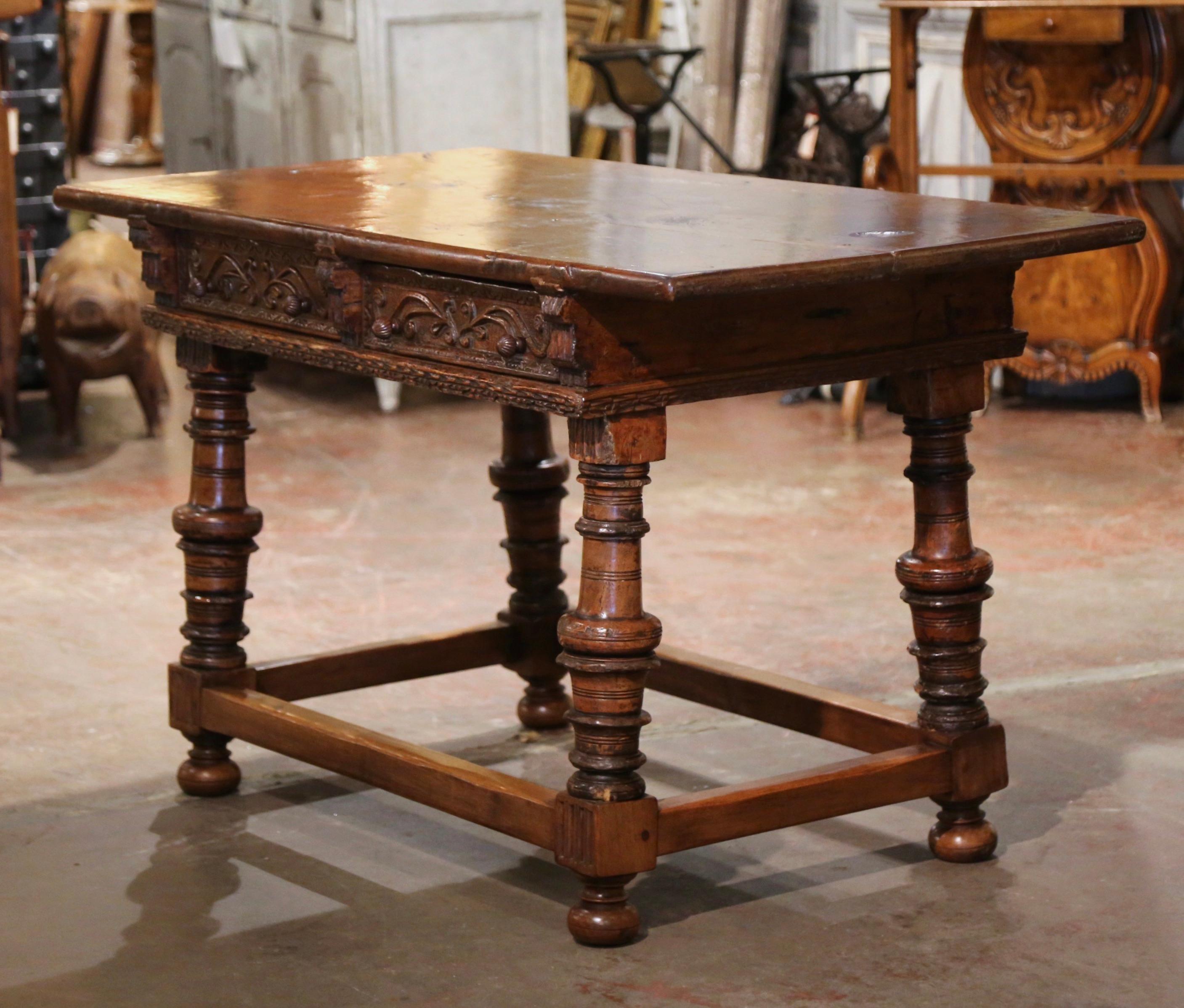 Crafted in Spain circa 1760, the antique writing table stands on thick carved turned legs ending with bun feet, and embellished with an elegant rectangular box stretcher at the base. The tall table features two hand carved drawers across the front