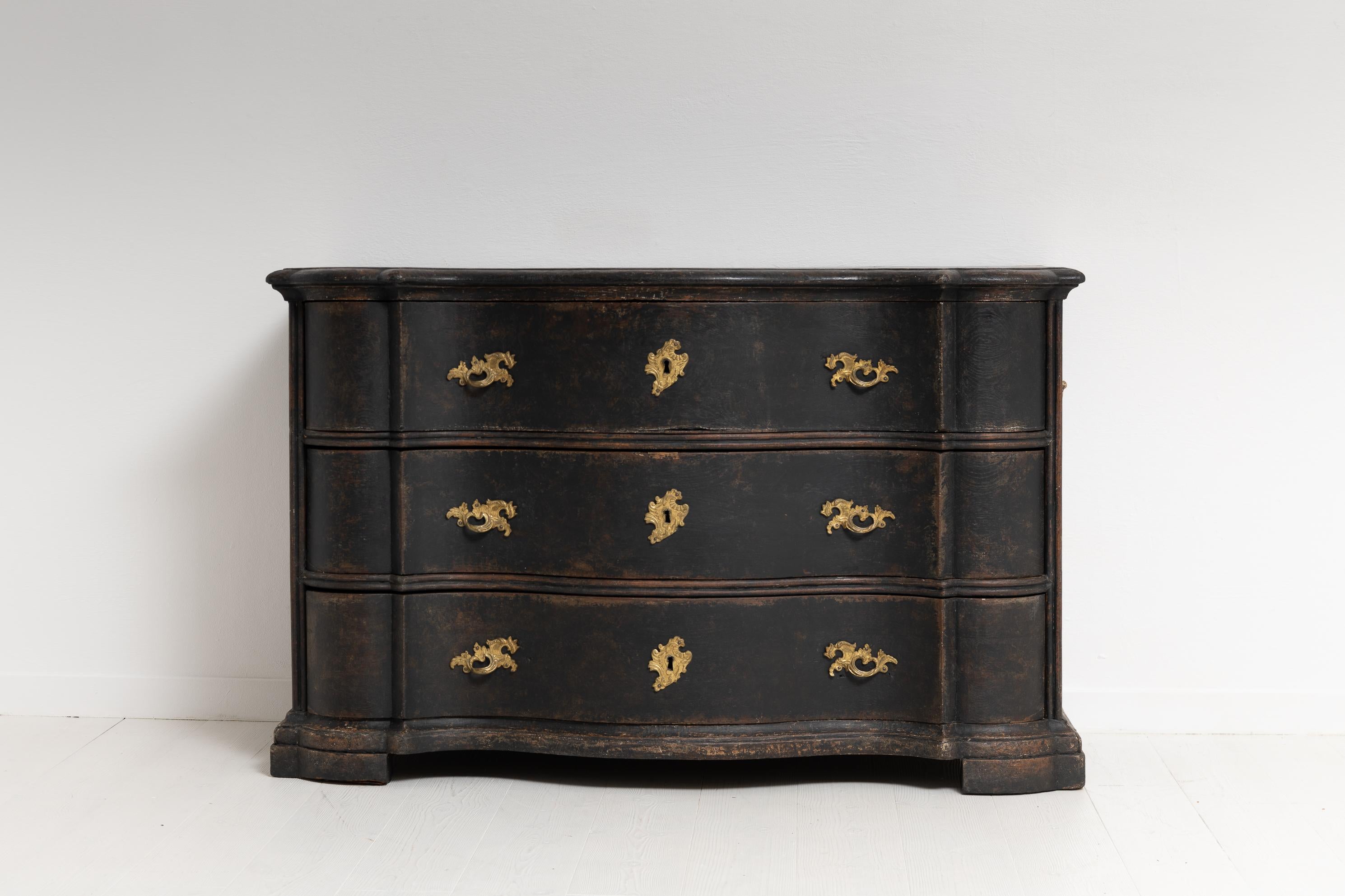 Black Swedish chest of drawers from the late baroque period. The chest is subtle but impactful with the dark paint, contrasting hardware and curved Baroque shape. It has three large curved drawers that all have the original locks. The key is
