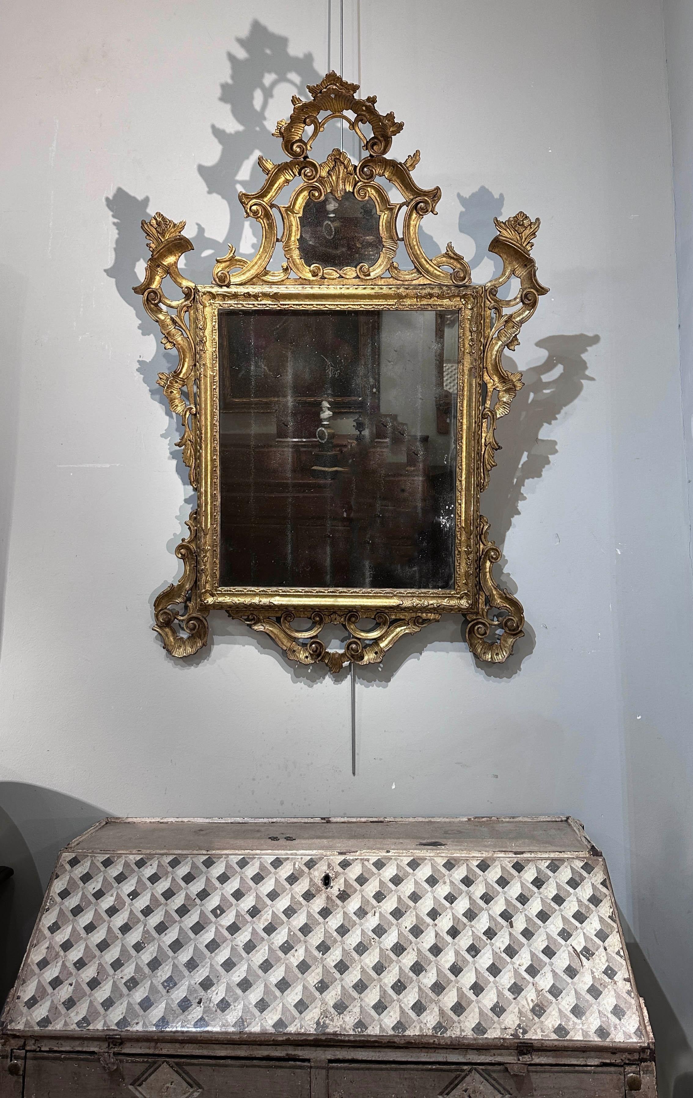 Splendid and refined mirror in carved pine wood and gilded with pure gold leaf. The frame features intricate patterns and floral curls that lend a touch of elegance and sophistication. The lights are original and a mirror panel adds further beauty