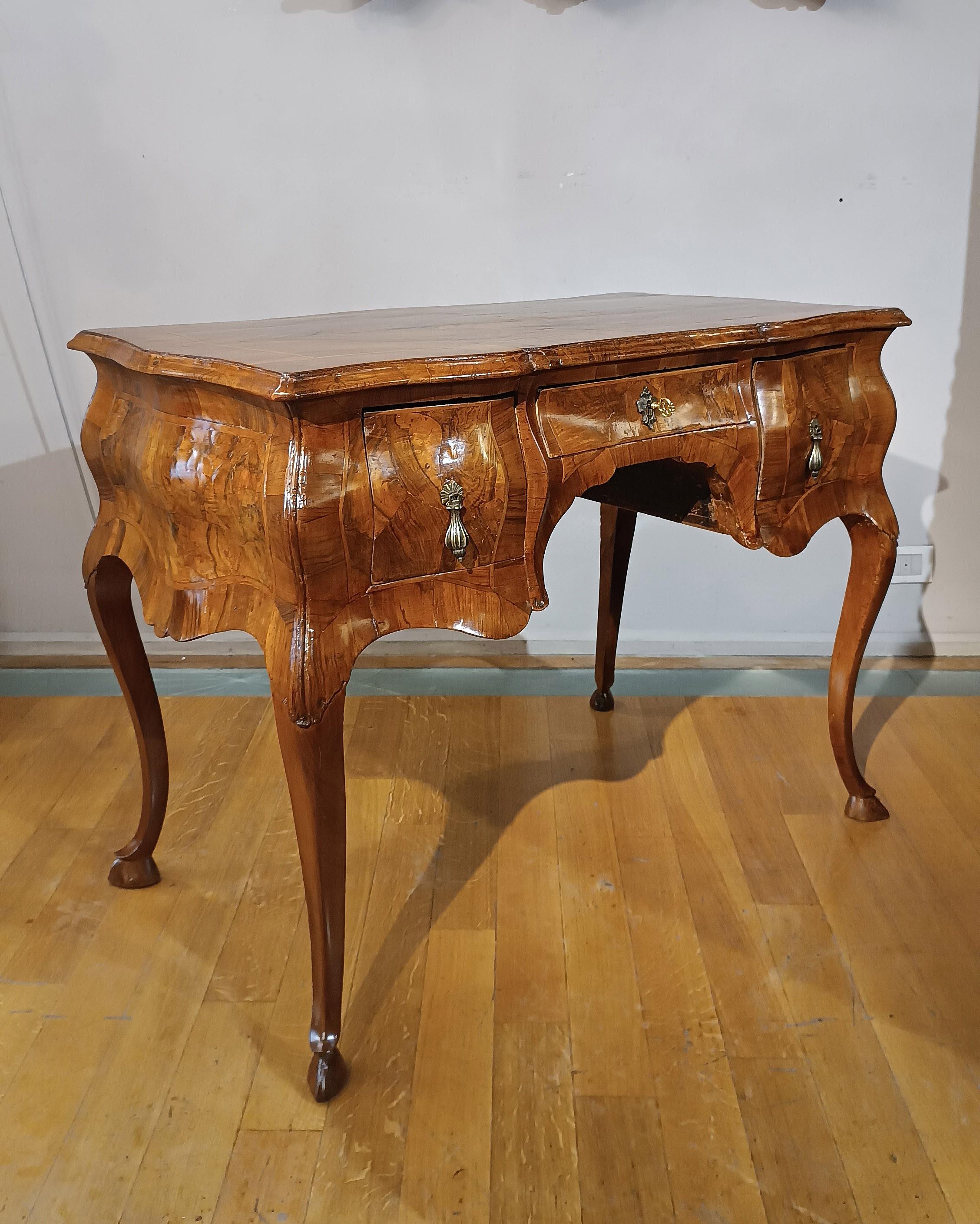 Elegant writing desk veneered entirely in walnut root. Its structure is completely wavy both on the top and on the sides, with sabre legs ending in feral feet. On the front there are three small ergonomic and opening drawers, equipped with handles