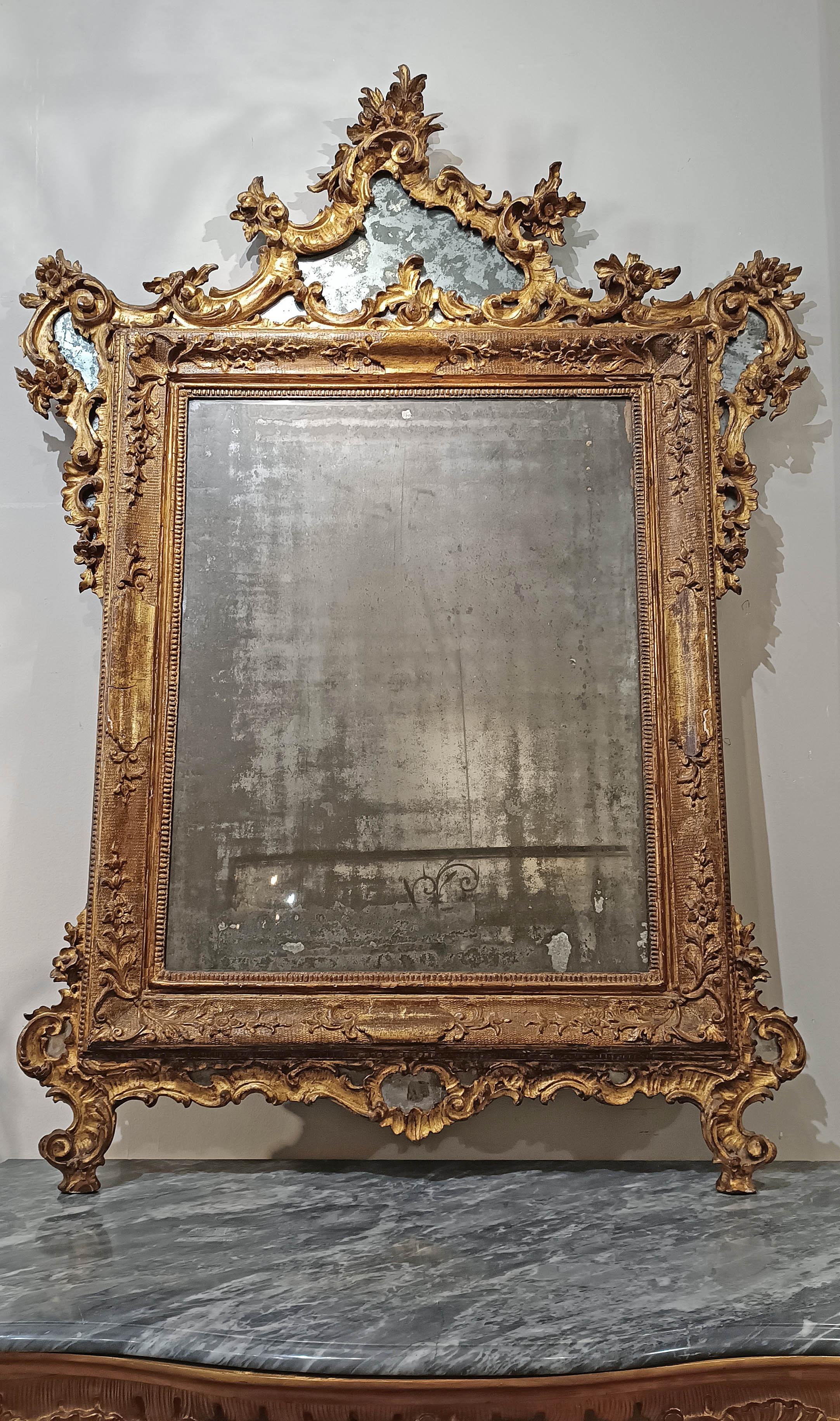 Elegant mirror made by Venetian artisans in the mid-18th century, fully following the Louis XV regency style. This mirror was made of carved pine wood and subsequently gilded with pure gold leaf, thus giving it a precious luminous effect, while the