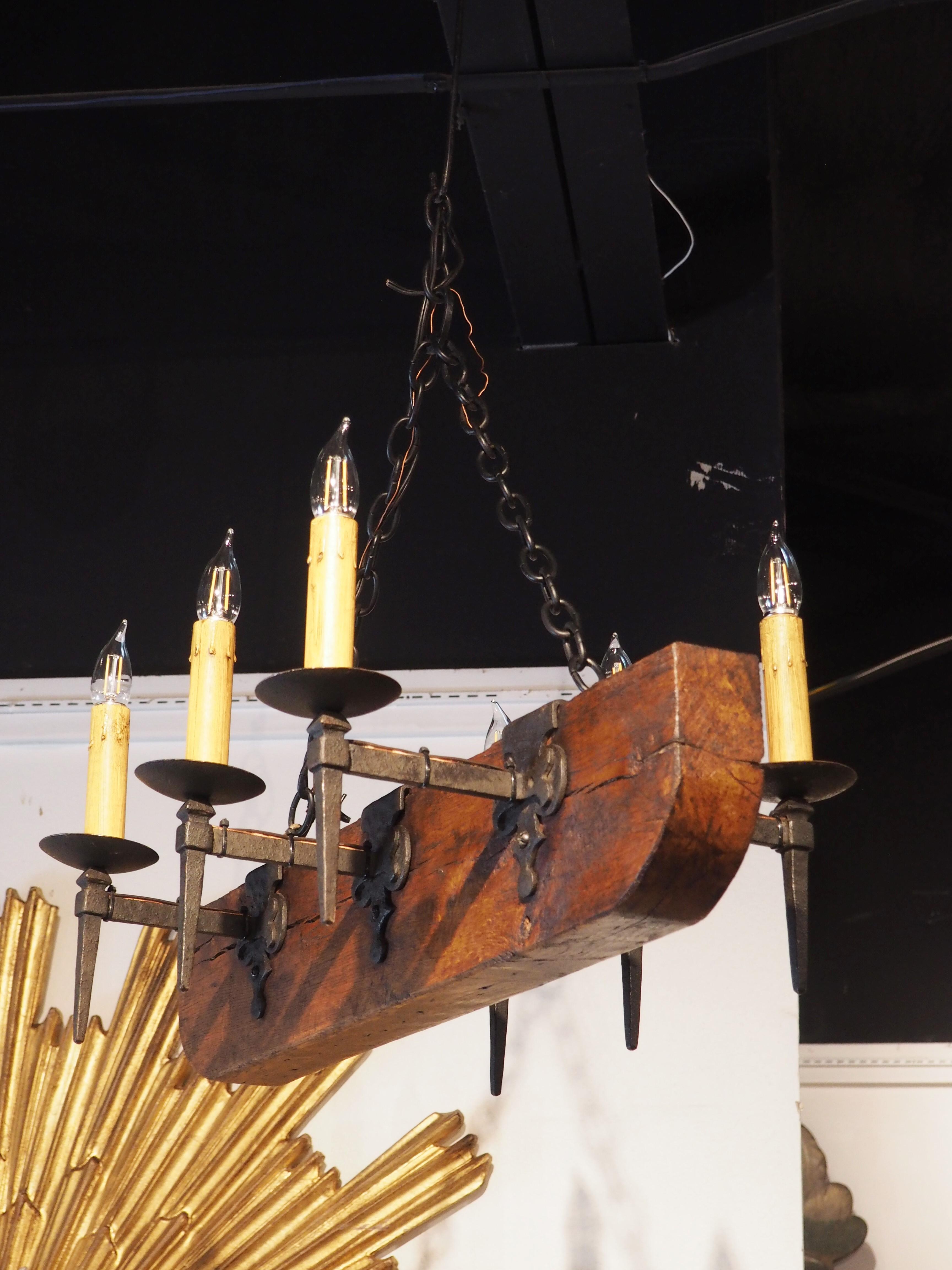 Constructed in France during the mid-1900s, the body of this six-light chandelier is comprised of a 6 5/8-inch thick 19th-century oak beam with a lovely golden brown patina. Each of the wrought iron arms has a black finish and extends roughly 8 ½