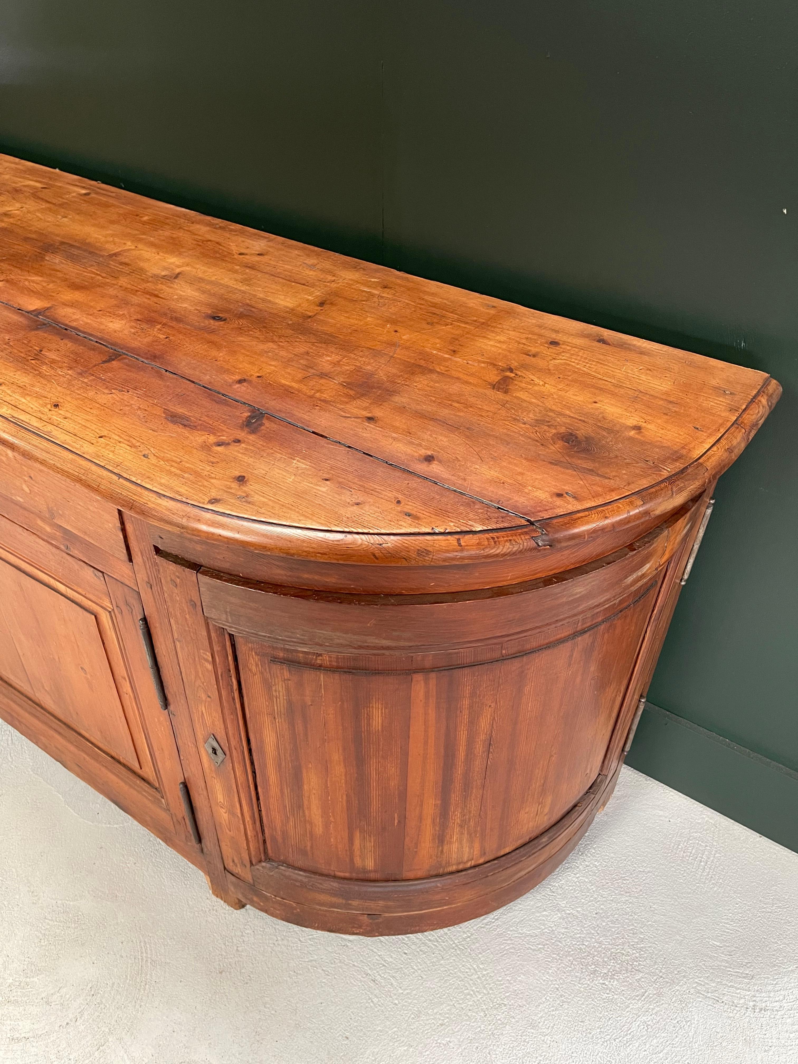 Embrace the allure of curves and timeless French craftsmanship with our Mid 19th-century French Savoyard Curved Sideboard made of pitch pine. From the picturesque region of Savoy, renowned for its artistry, this piece piece marries the refined