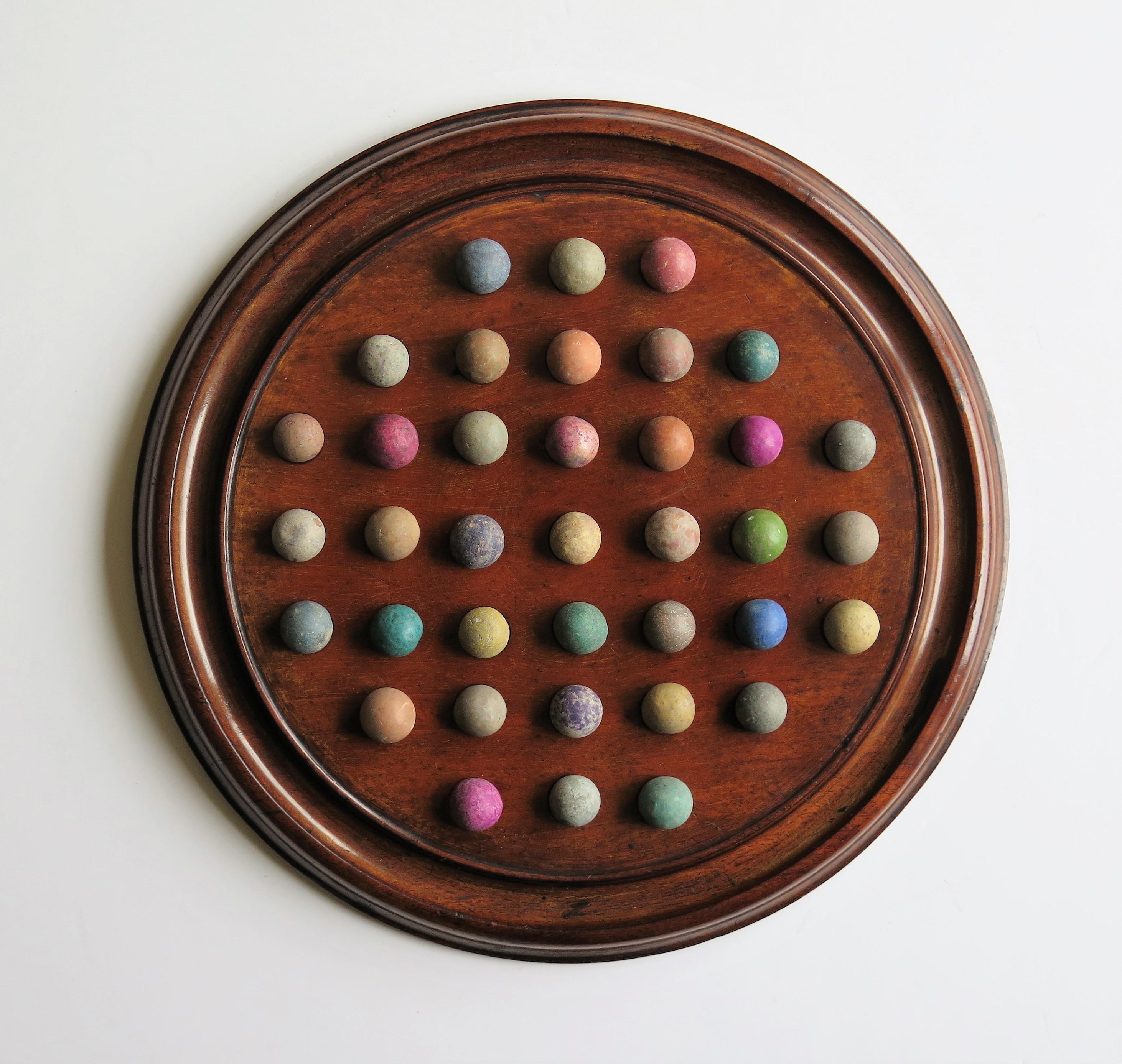 This is a complete Marble Solitaire game, having a beautiful Mahogany board and a complete set of 37 clay or stone handmade marbles, all dating to the mid-19th century Victorian period.
 
This board is a really good example. It is circular and