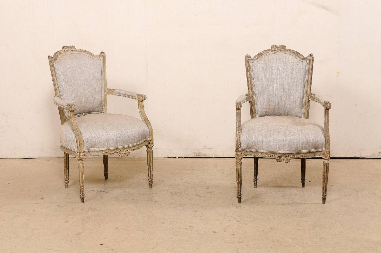 A French pair of carved wood armchairs, with upholstered seat and back, from the mid 19th century. This pair of antique chairs from France, are hand-carved in the Louis XVI style, each having a beautifully carved arched top rail, flanked within