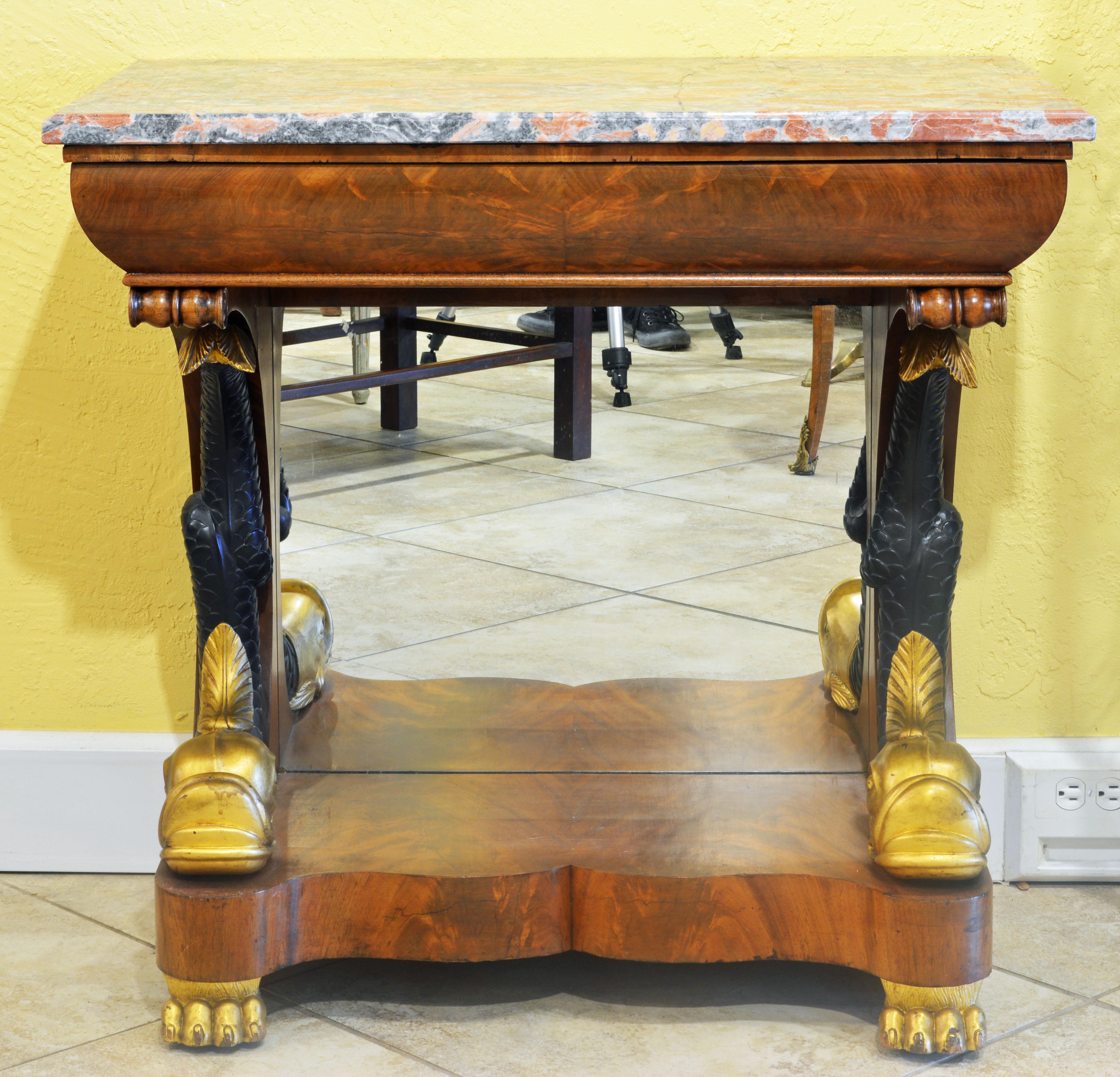 This great console table features a Siena marble top above a curved frieze fashioned as a drawer. It rests on two elaborately carved upswung dolphins with gilt heads and ebonized tails sitting with a mirrored back panel on the shaped base and gilt