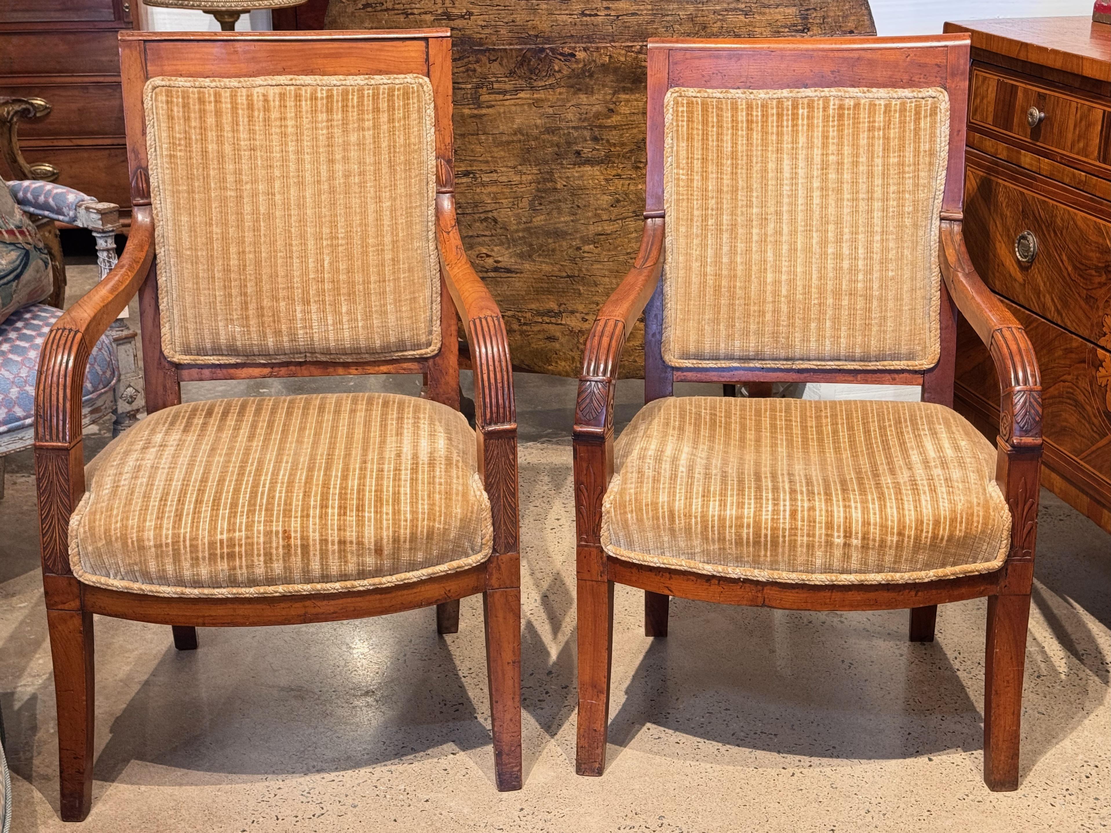 Bellissima coppia di sedie a bracci aperti in stile Impero con schienale quadrato e braccioli intagliati e scanalati. Rivestita in velluto a righe vintage, ogni sedia presenta dettagliati intagli a mano sui terminali dei bracci e sui supporti