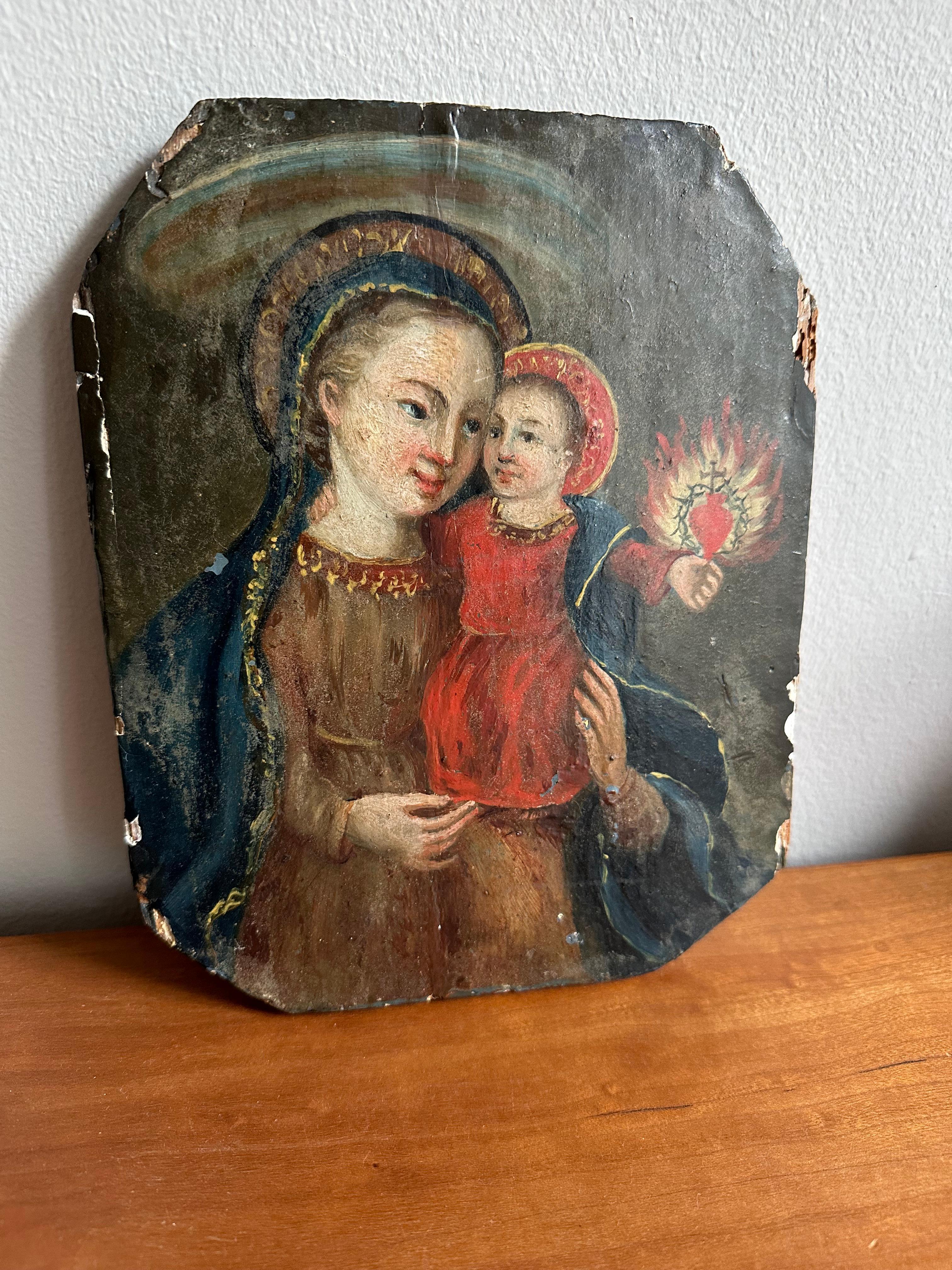 This remarkable mid-19th century alpine oil painting on wood captures a Madonna and Child in a deeply symbolic composition. The child holds a flaming heart adorned with a crown of thorns and a cross, evoking themes of love, sacrifice, and devotion