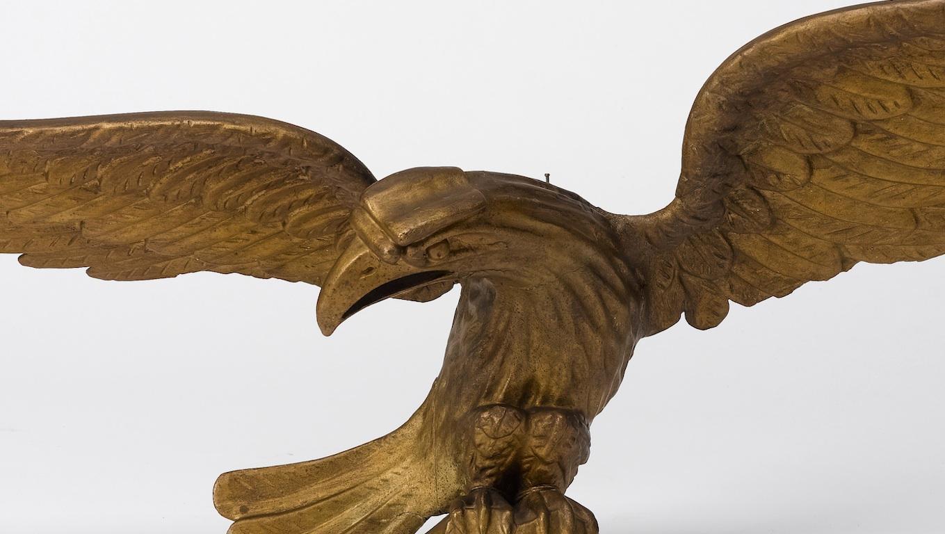 This is a giltwood hand-carved American eagle, circa mid-19th century. Depicted with its wings fully spread and feathers carved in fine detail. The eagle's form is nearly in the round with its outreaching head turned to the right. Its tail is