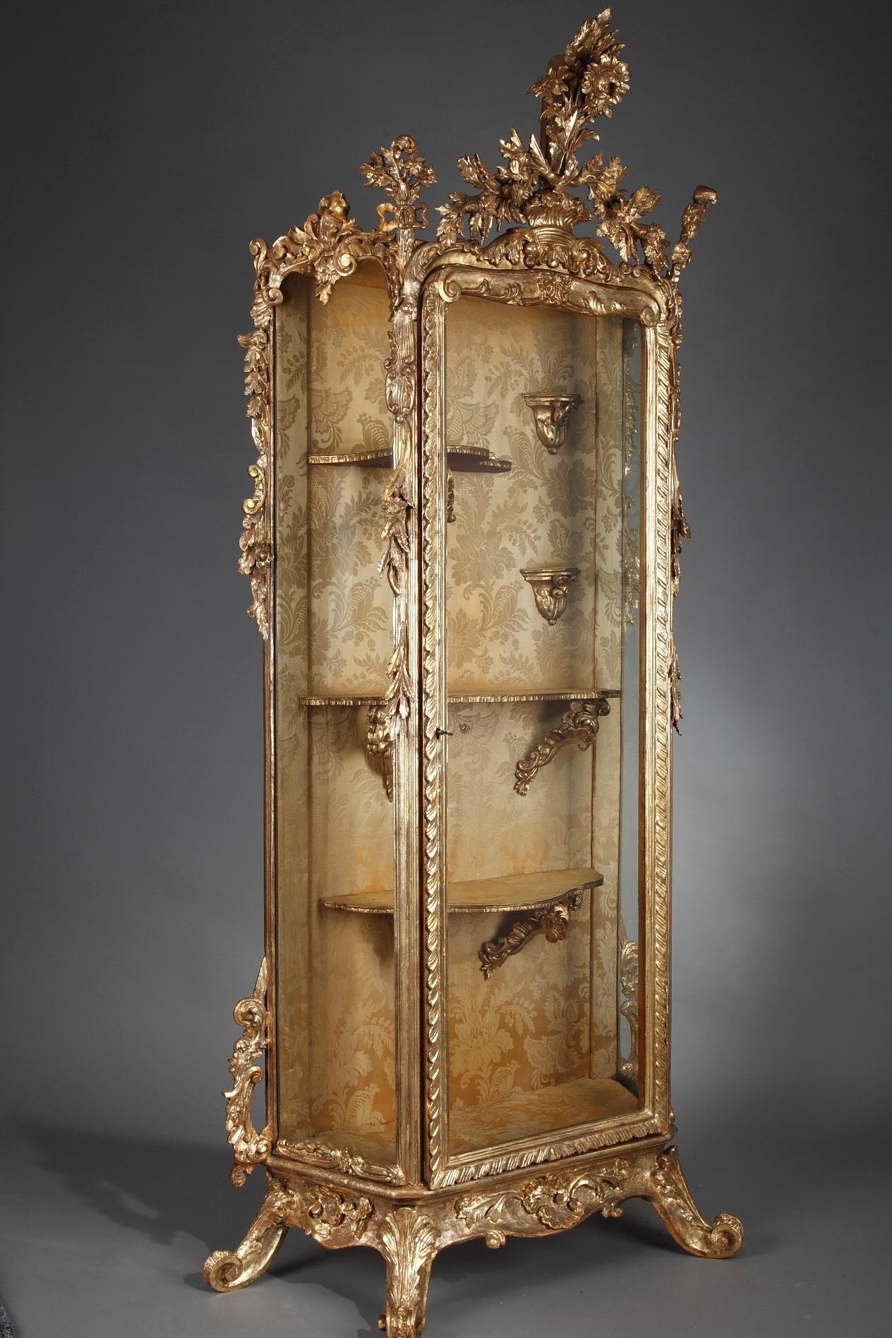 This large exquisite vitrine crafted in Italy in the mid-19th century displays the opulence of Baroque style. The display cabinet is richly decorated by beautifully sculpted giltwood mounts of floral garlands, rocaille, foliage and scrolls. The