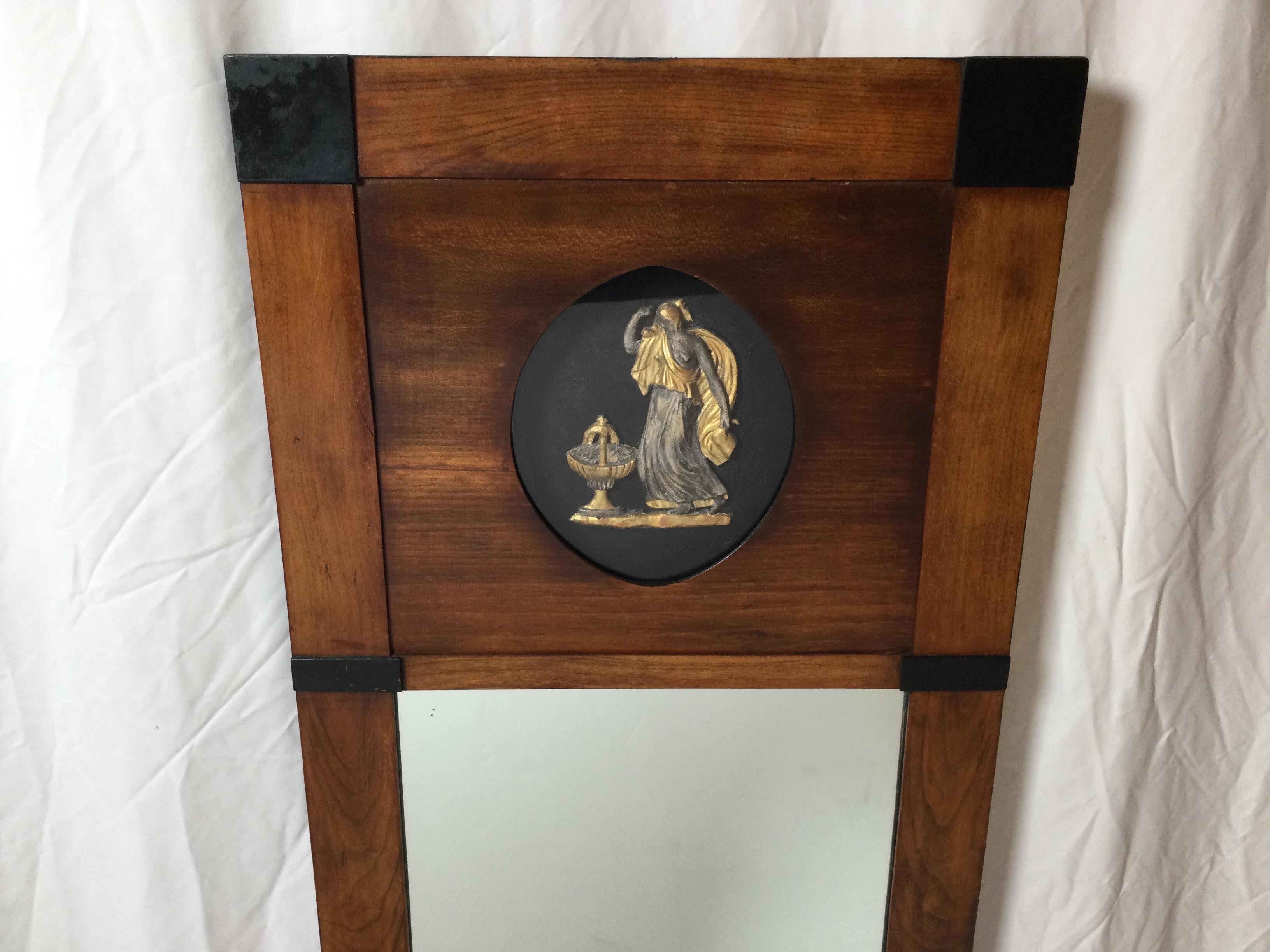 The slender mirror with a recently french polished mahogany frame with a high relief cartouche of a neoclassical draped lady. The frame with ebonized wood accents. The mirror has been replaced.